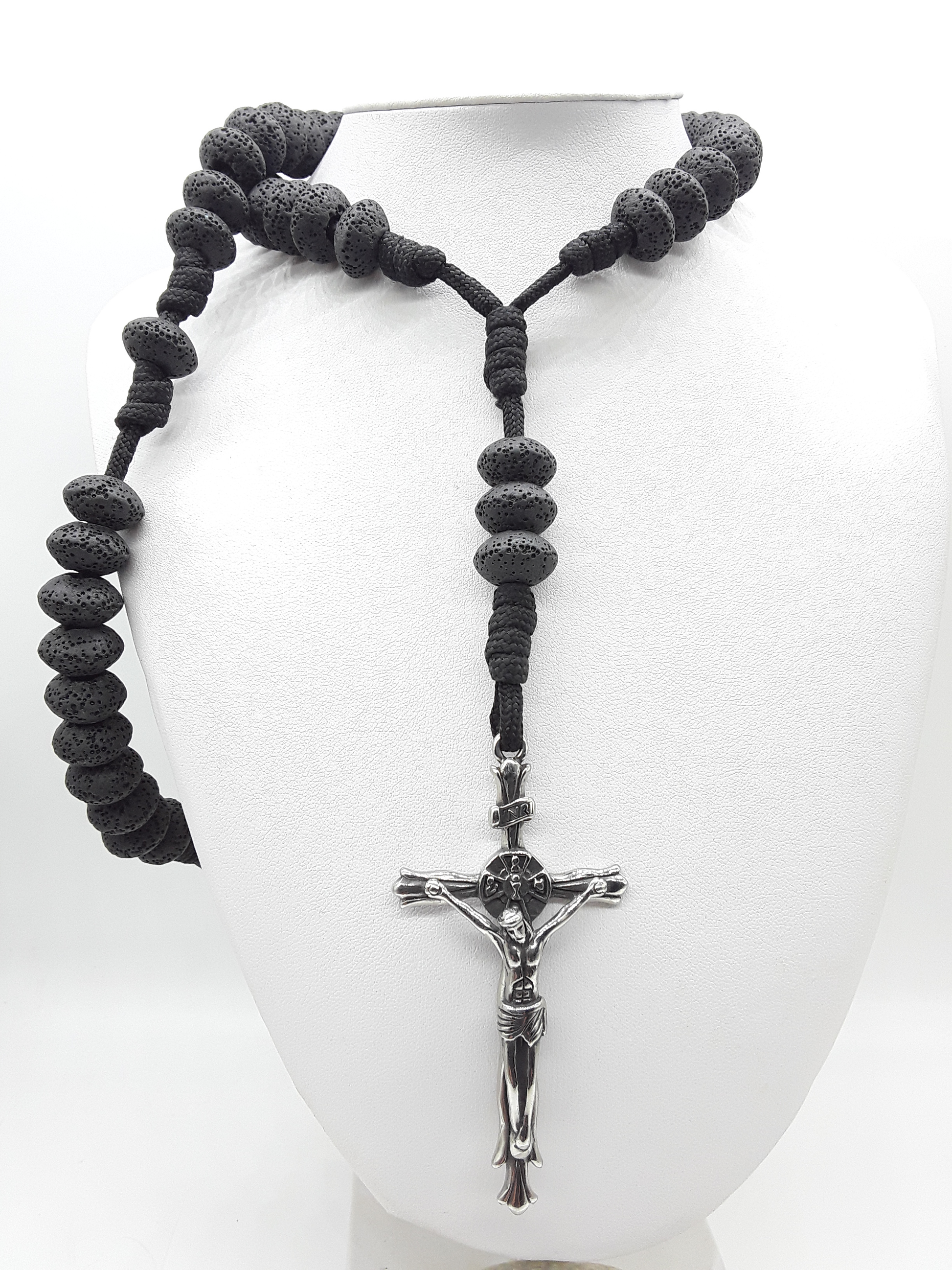 Lava Stone Paracord Catholic Rosary with stainless steel crucifix by Polmadeva resting on a white mannequin.