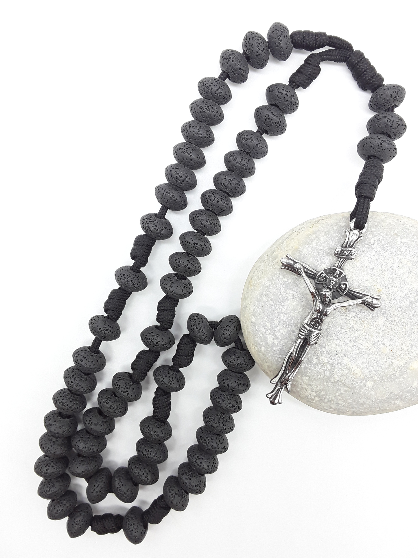 Lava Stone Paracord Catholic Rosary with stainless steel crucifix by Polmadeva resting on natural stone surface.