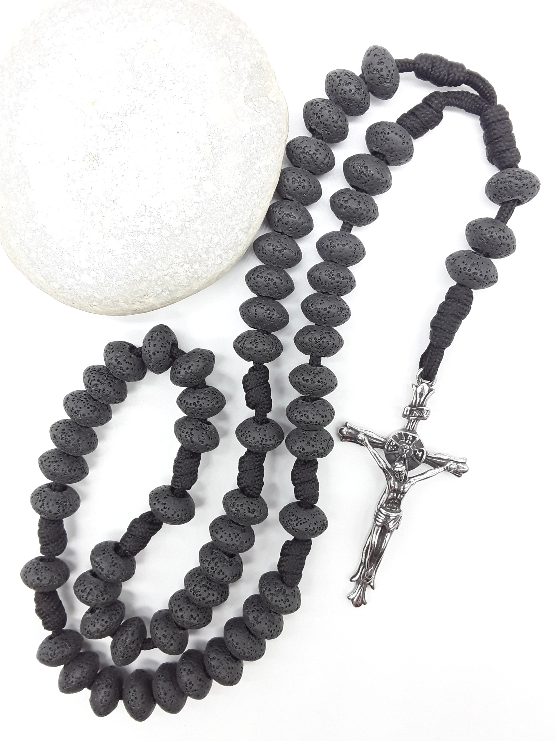 Lava Stone Paracord Catholic Rosary with stainless steel crucifix by Polmadeva placed beside natural stone, 5-decade design.