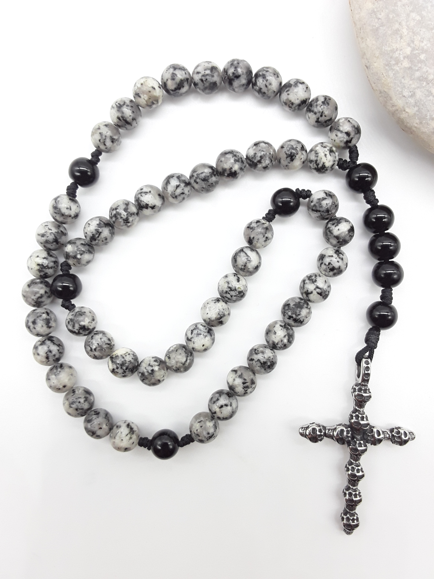 Handheld Catholic rosary with jasper and black onyx beads placed beside natural stone, stainless steel cross visible.