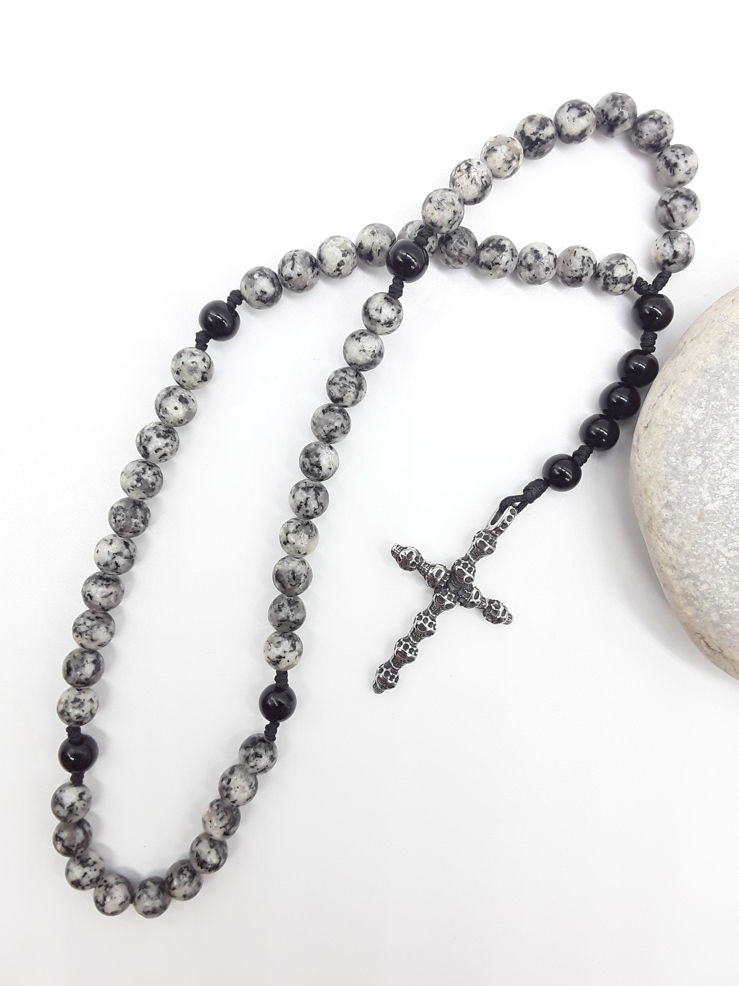 Handheld Catholic rosary with jasper and black onyx beads placed beside natural stone, stainless steel cross visible.
