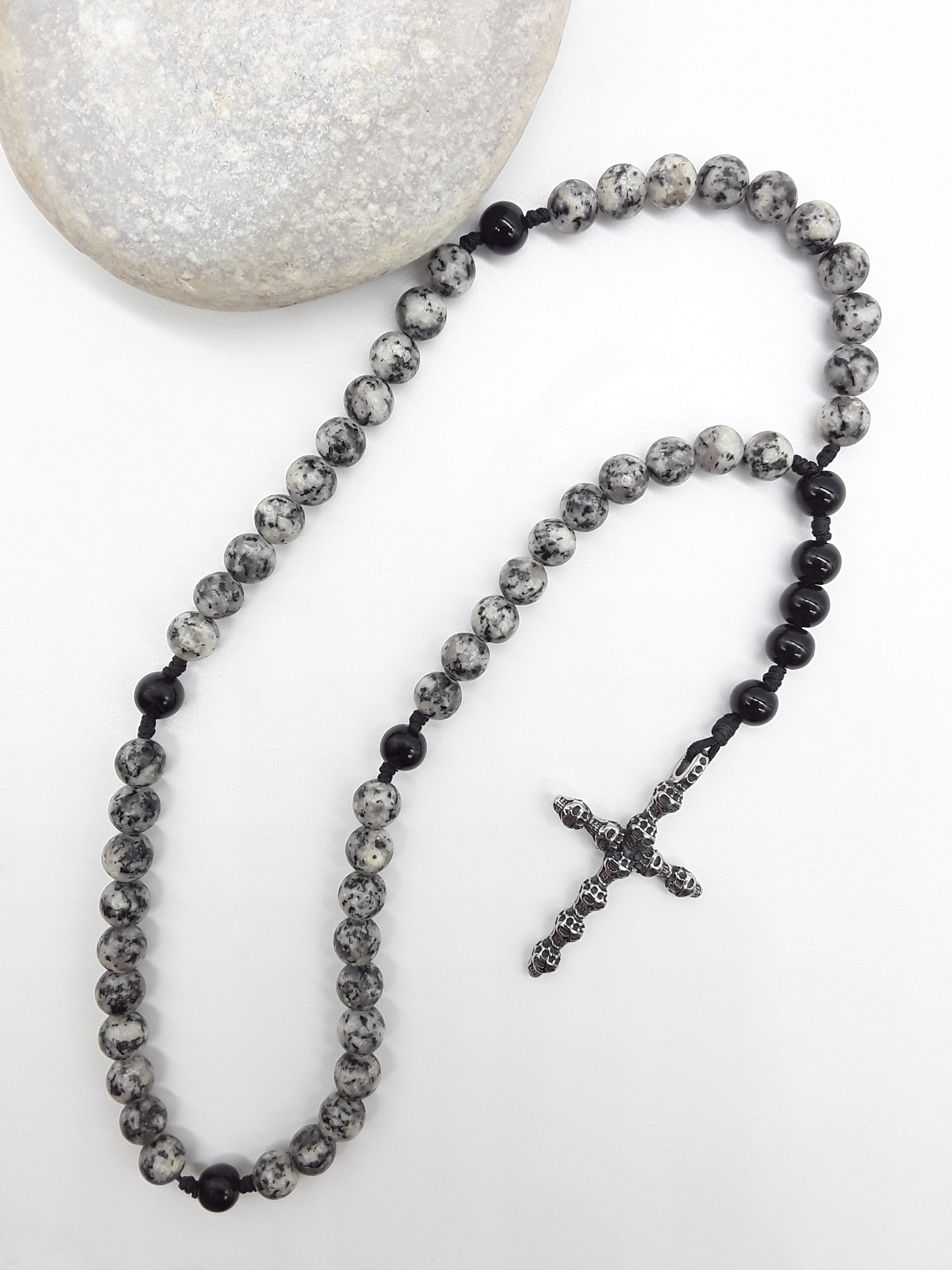 Handheld Catholic rosary with jasper and black onyx beads placed beside natural stone, stainless steel cross visible.