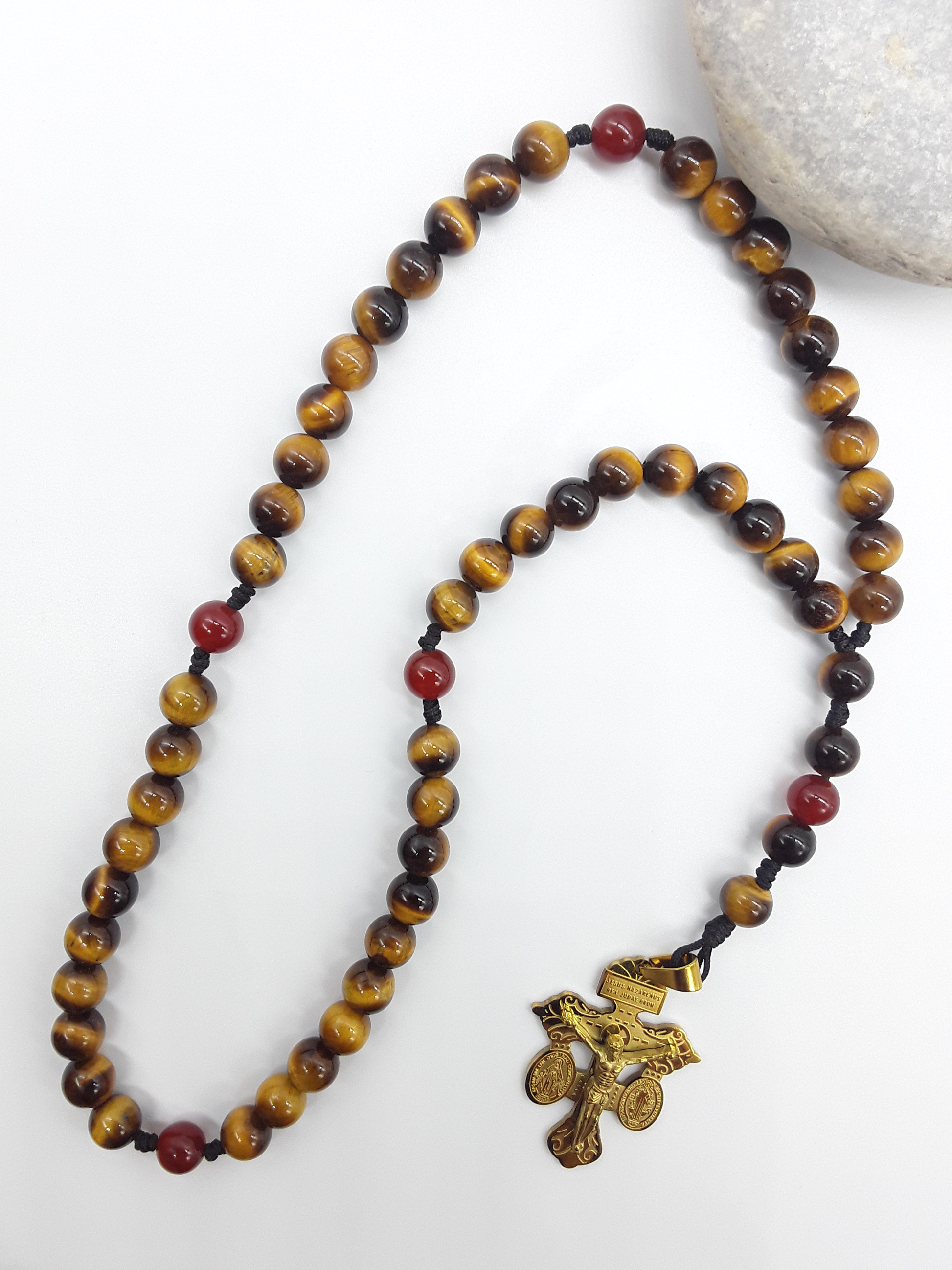 Pocket Catholic Rosary with Tiger’s Eye and Carnelian beads placed beside natural stone, featuring a steel devotional crucifix