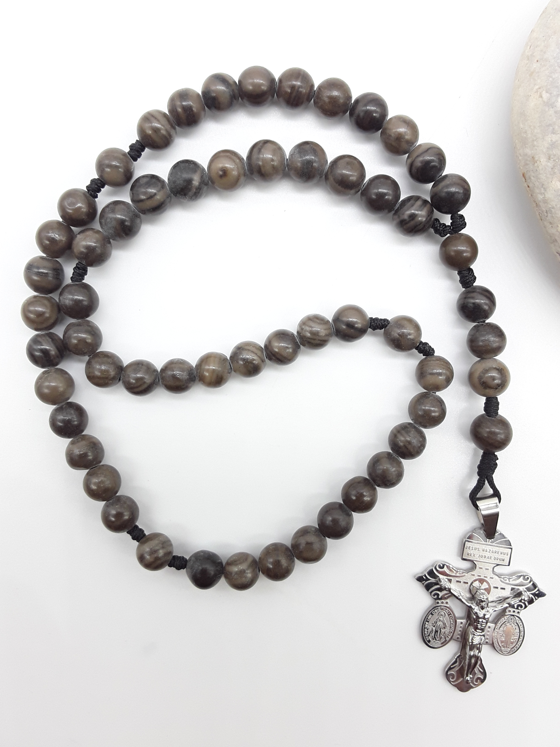 Black Wood Lace Stone pocket Catholic rosary with stainless steel crucifix placed beside a natural stone on a white surface.