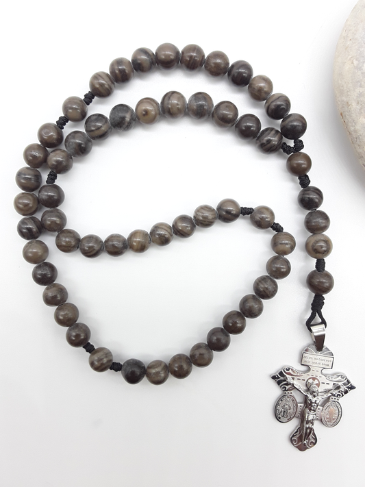 Black Wood Lace Stone pocket Catholic rosary with stainless steel crucifix placed beside a natural stone on a white surface.