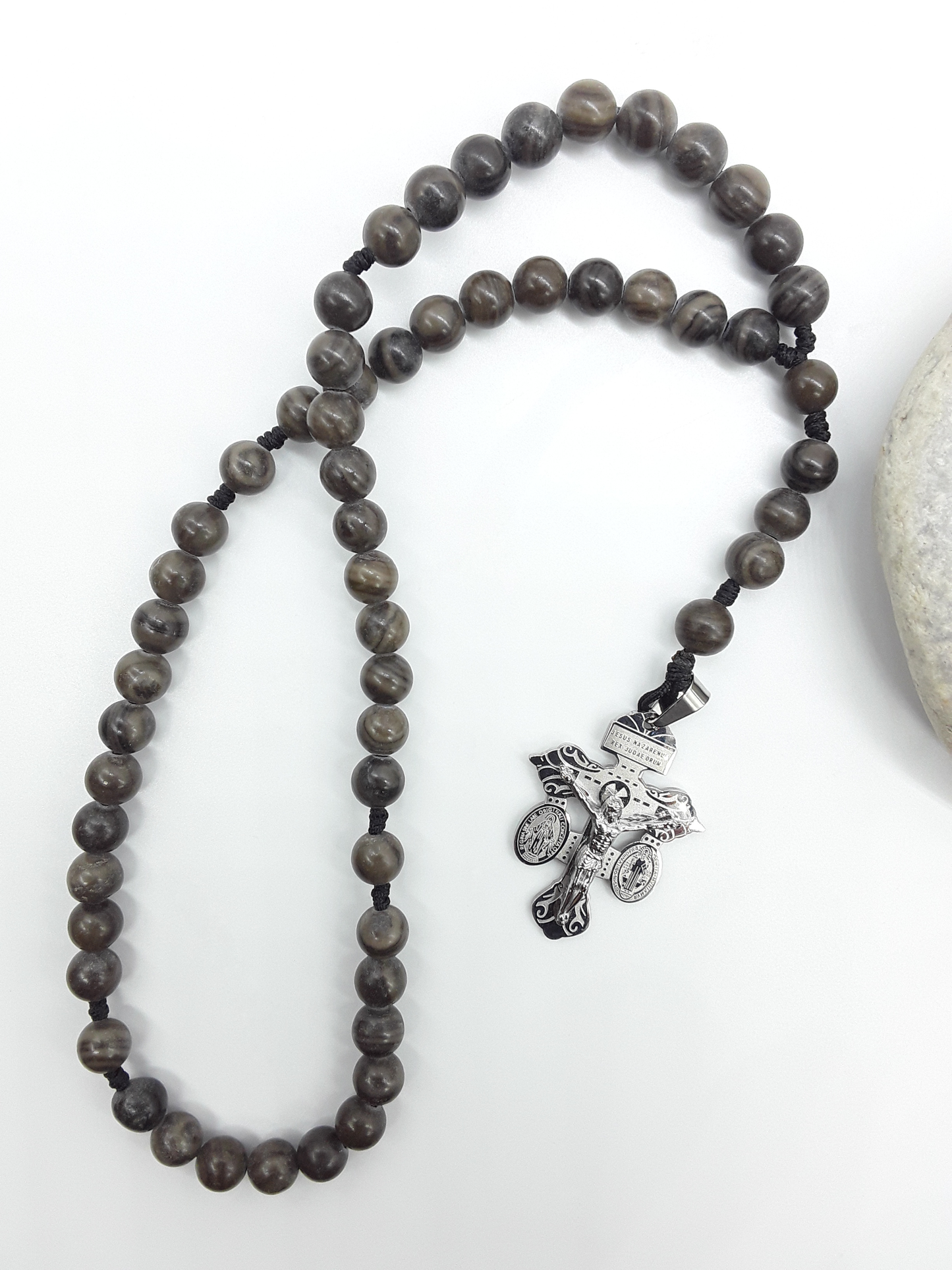 Black Wood Lace Stone pocket Catholic rosary with stainless steel crucifix placed beside a natural stone on a white surface.