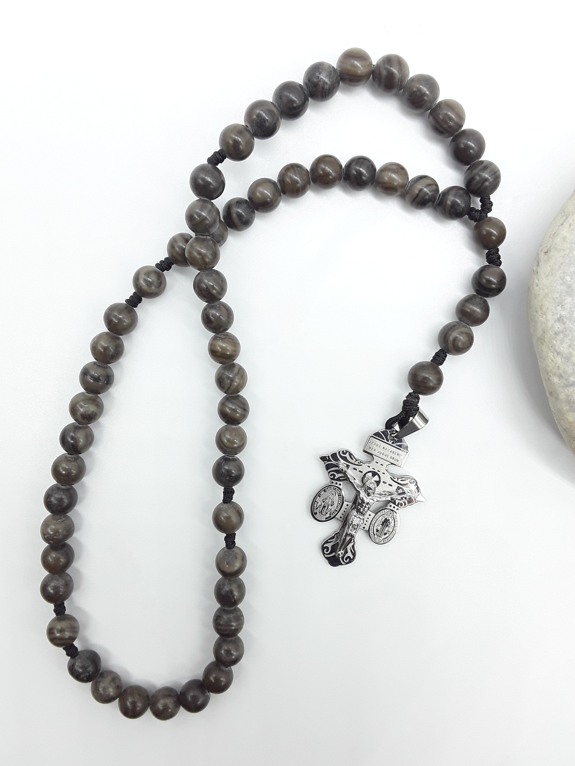 Black Wood Lace Stone pocket Catholic rosary with stainless steel crucifix placed beside a natural stone on a white surface.