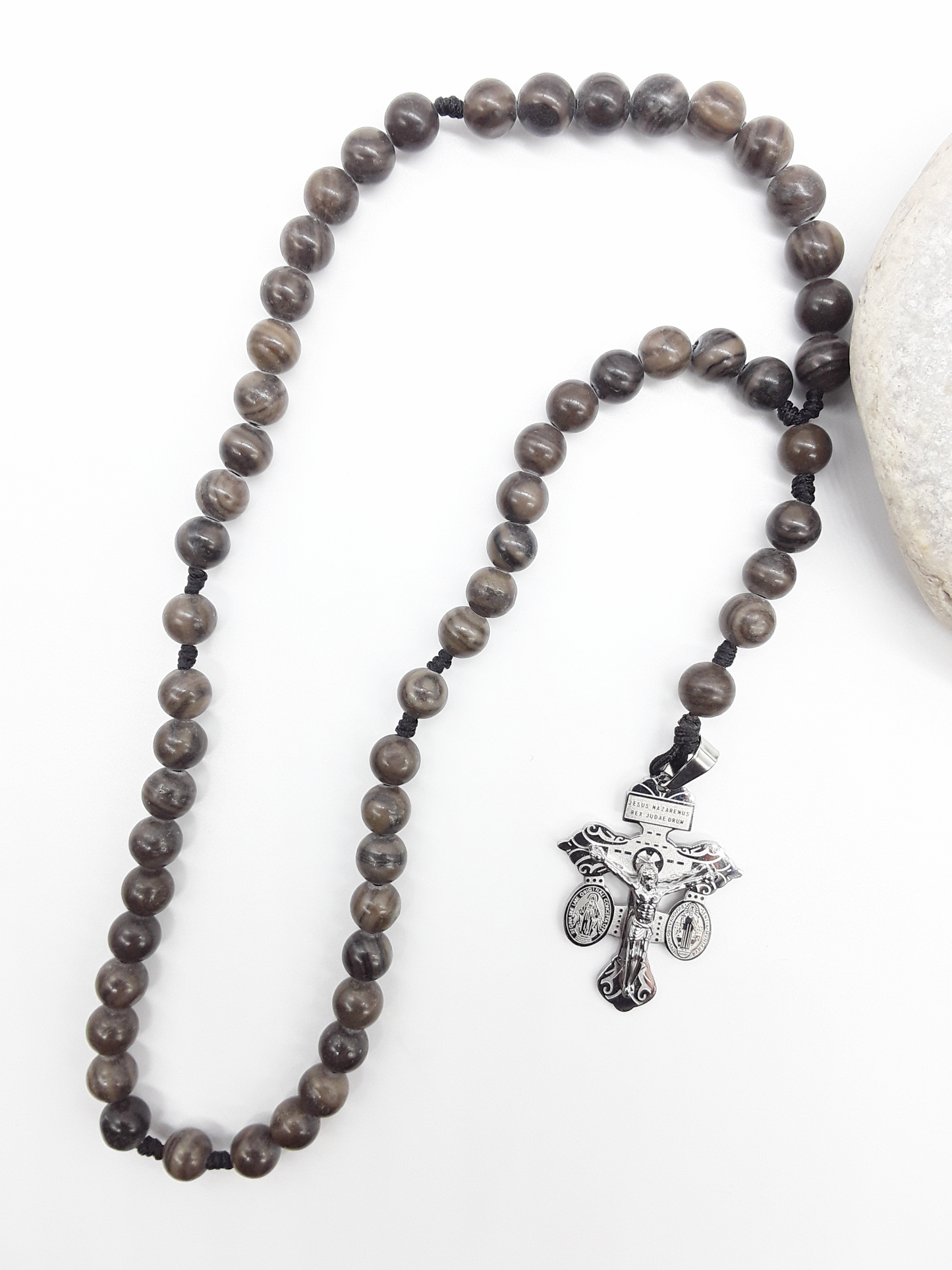 Black Wood Lace Stone pocket Catholic rosary with stainless steel crucifix placed beside a natural stone on a white surface.