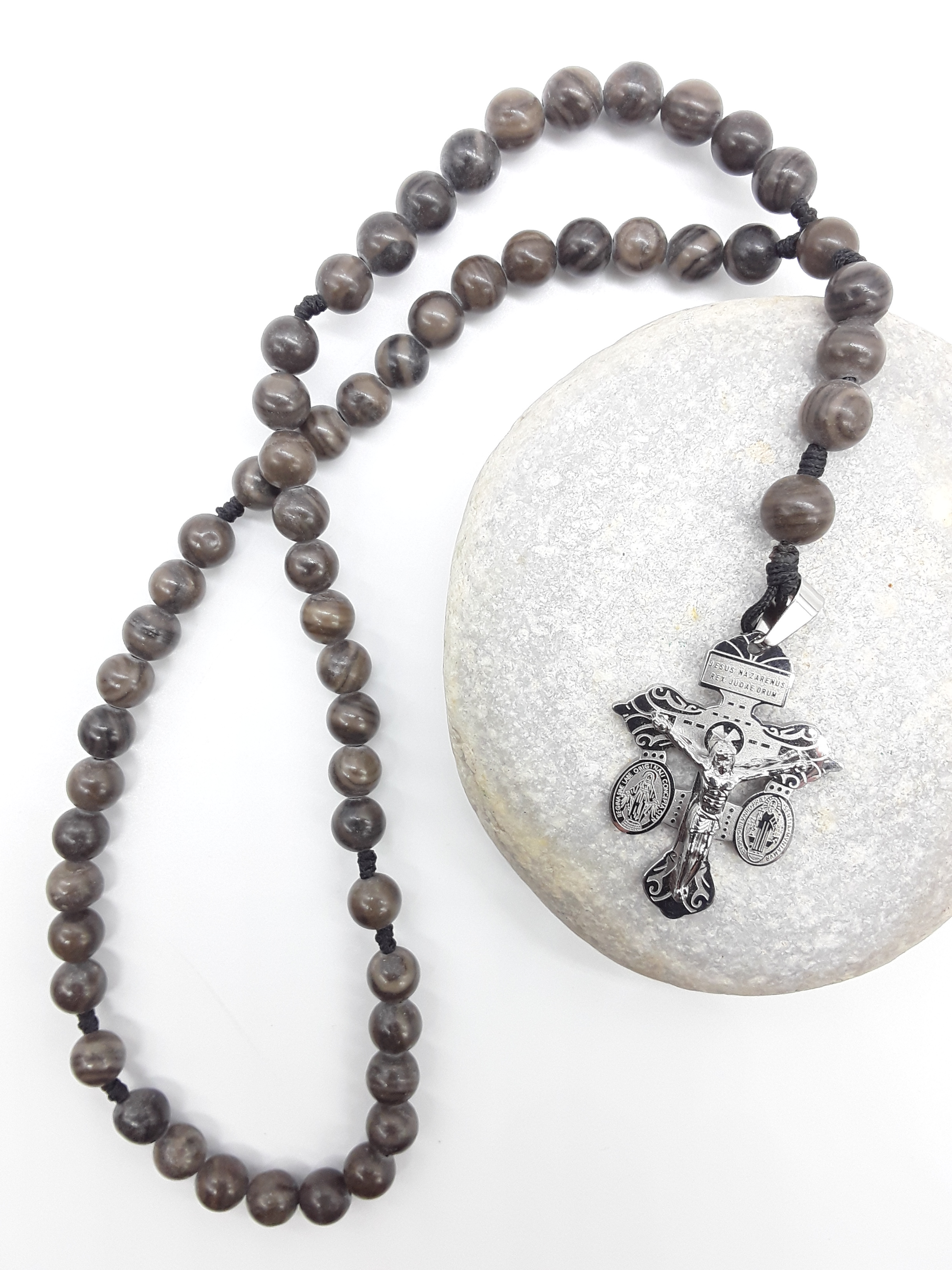 Pocket Catholic rosary made of Black Wood Lace Stone beads with a stainless steel crucifix resting on a natural stone.