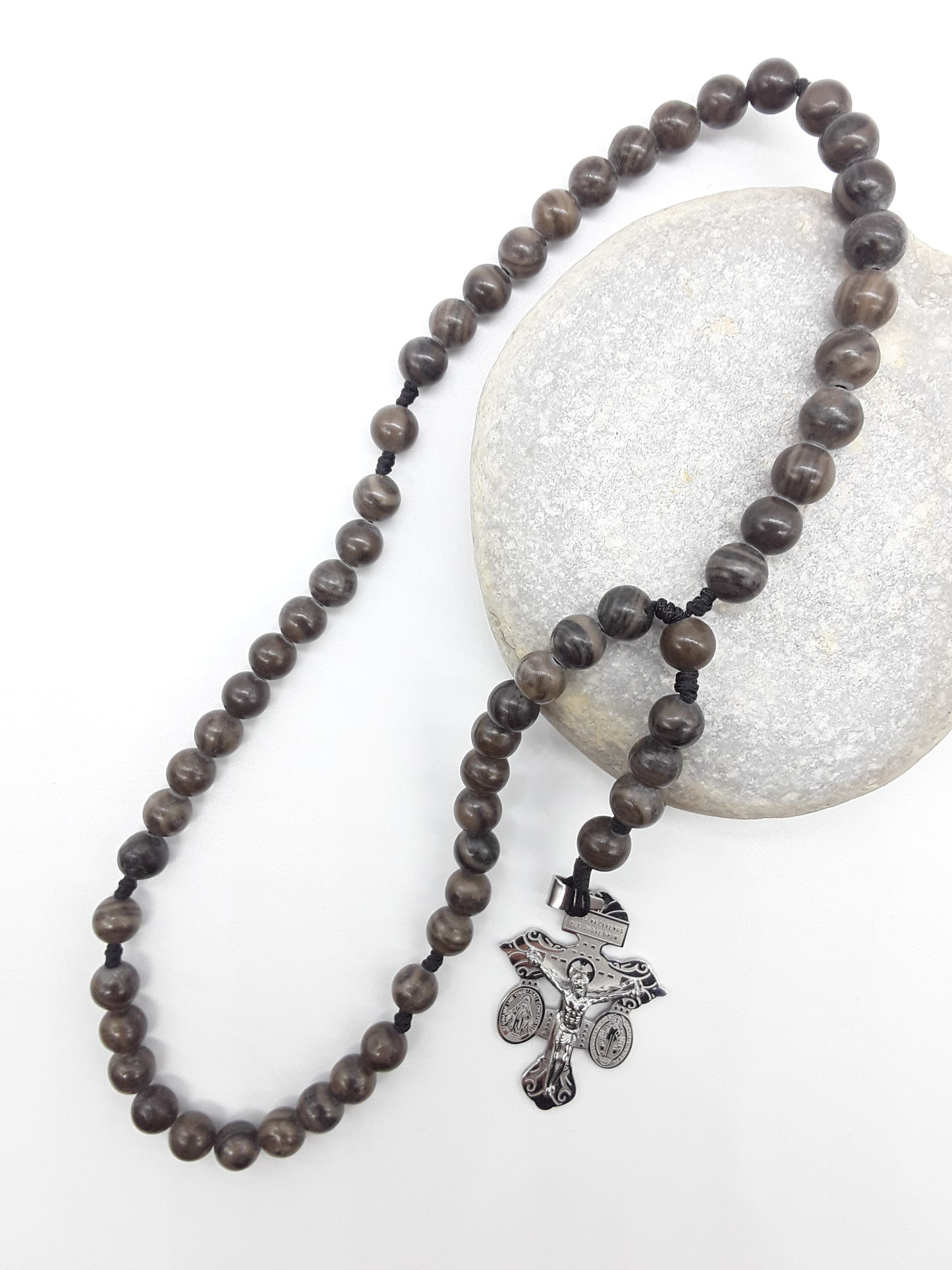 Pocket Catholic rosary made of Black Wood Lace Stone beads with a stainless steel crucifix resting on a natural stone.