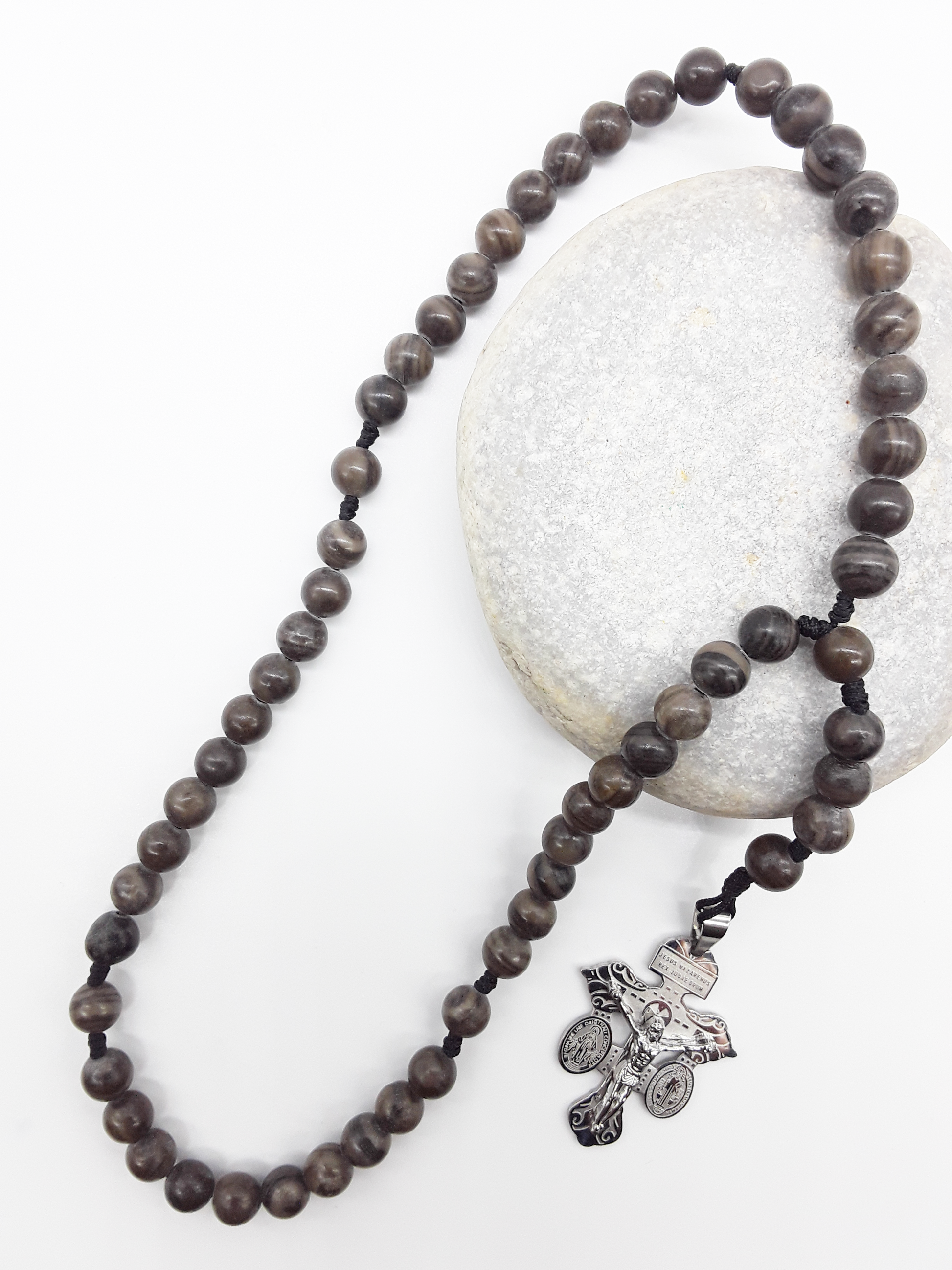 Pocket Catholic rosary made of Black Wood Lace Stone beads with a stainless steel crucifix resting on a natural stone.