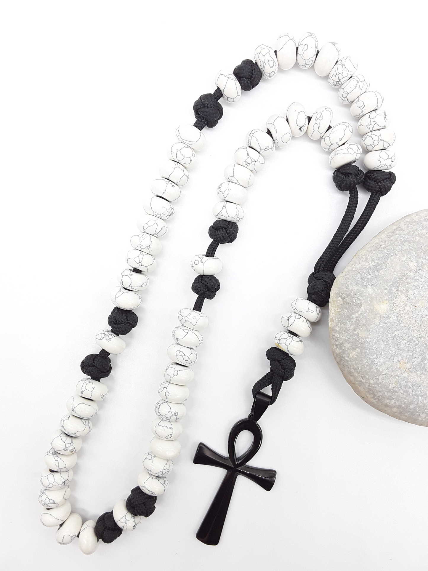 Howlite Paracord Catholic Rosary with Ankh cross by Polmadeva placed beside natural stone, 5-decade design.