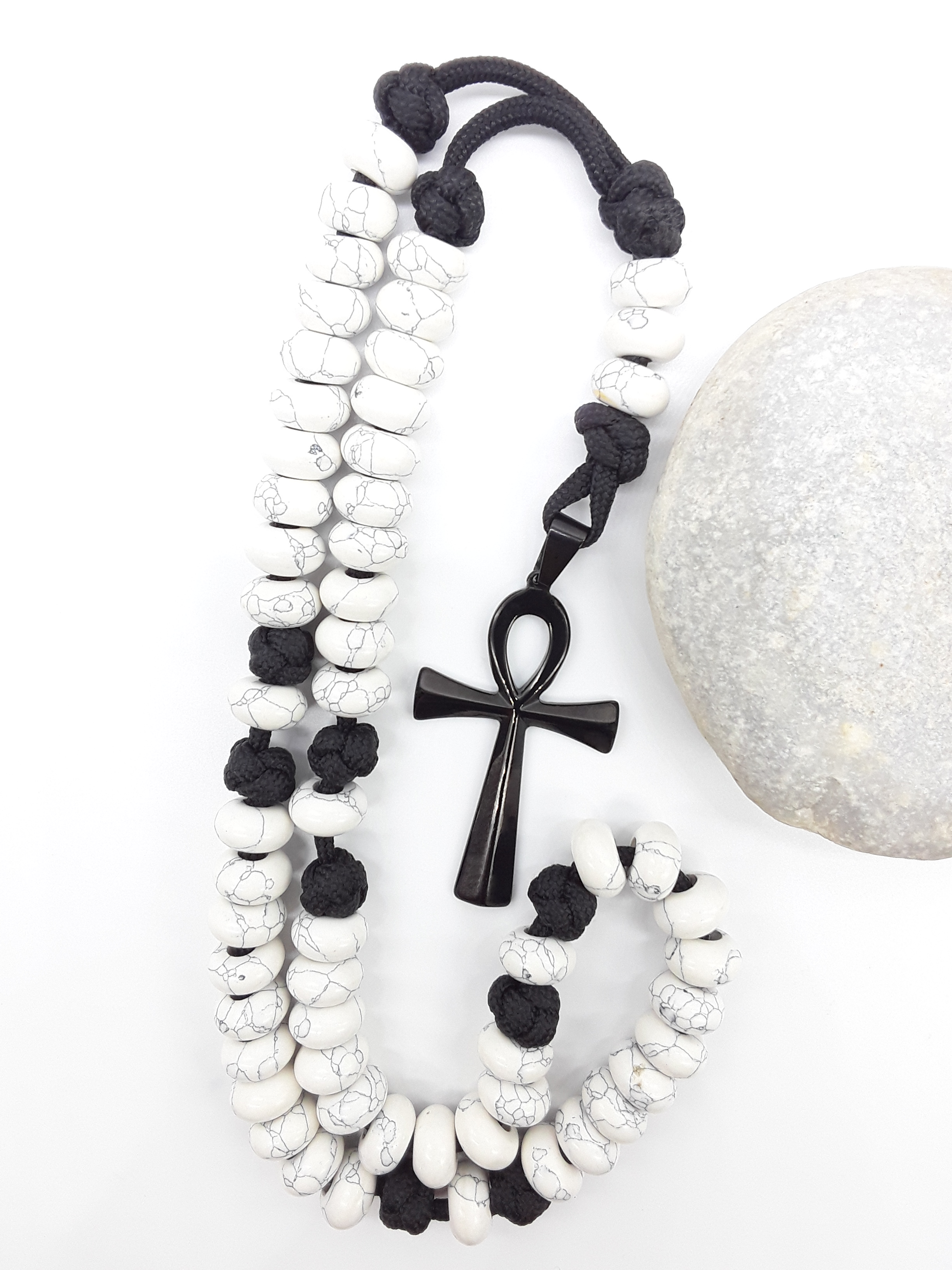 Howlite Paracord Catholic Rosary with Ankh cross by Polmadeva placed beside natural stone, 5-decade design.