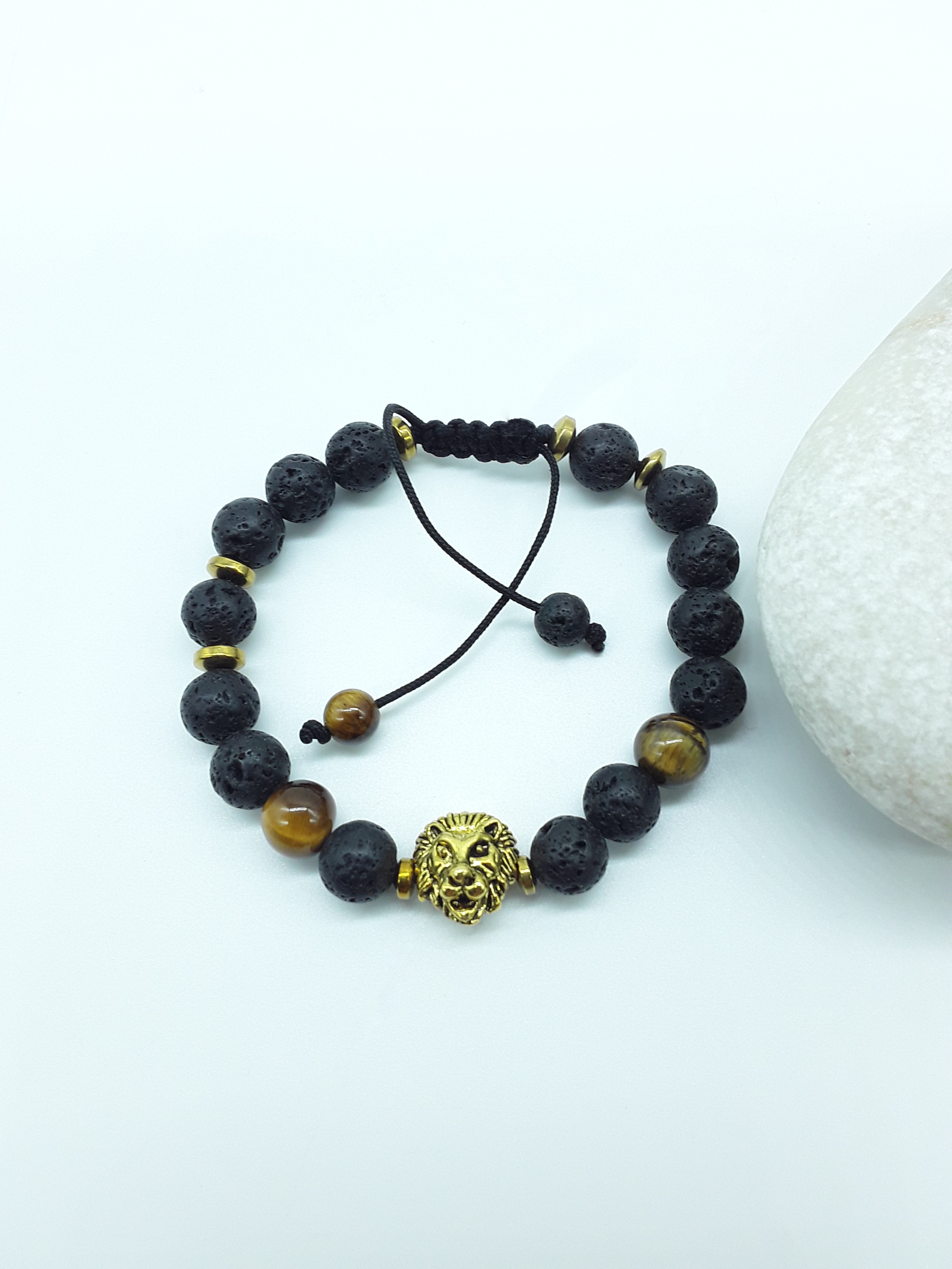 Holdfast beaded bracelet with lion symbol resting on natural stone placed beside stone, grounded minimalist composition