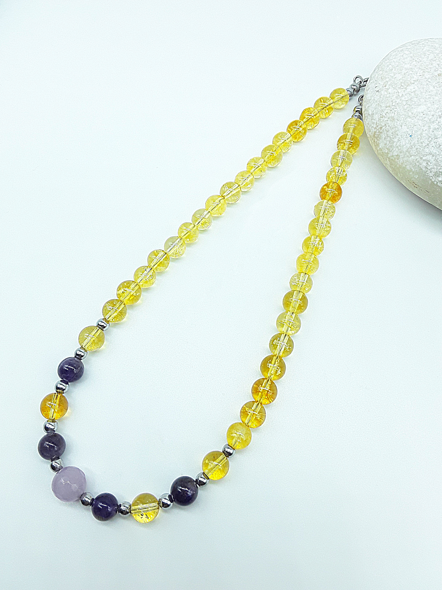 Luminous Ascent Necklace by Polmadeva with citrine, amethyst, rose quartz and hematite gemstones, photographed on a natural stone.