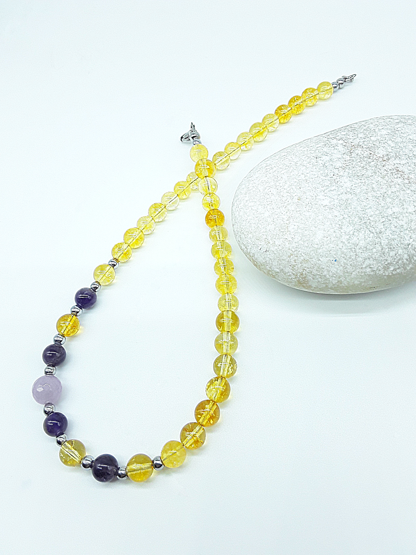 Luminous Ascent Necklace by Polmadeva with citrine, amethyst, rose quartz and hematite gemstones, arranged on a natural stone.