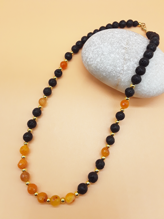 Our Place Agate, Lava Stone and Hematite necklace with gold-plated Stainless Steel clasp by POLMADEVA next to a white stone.
