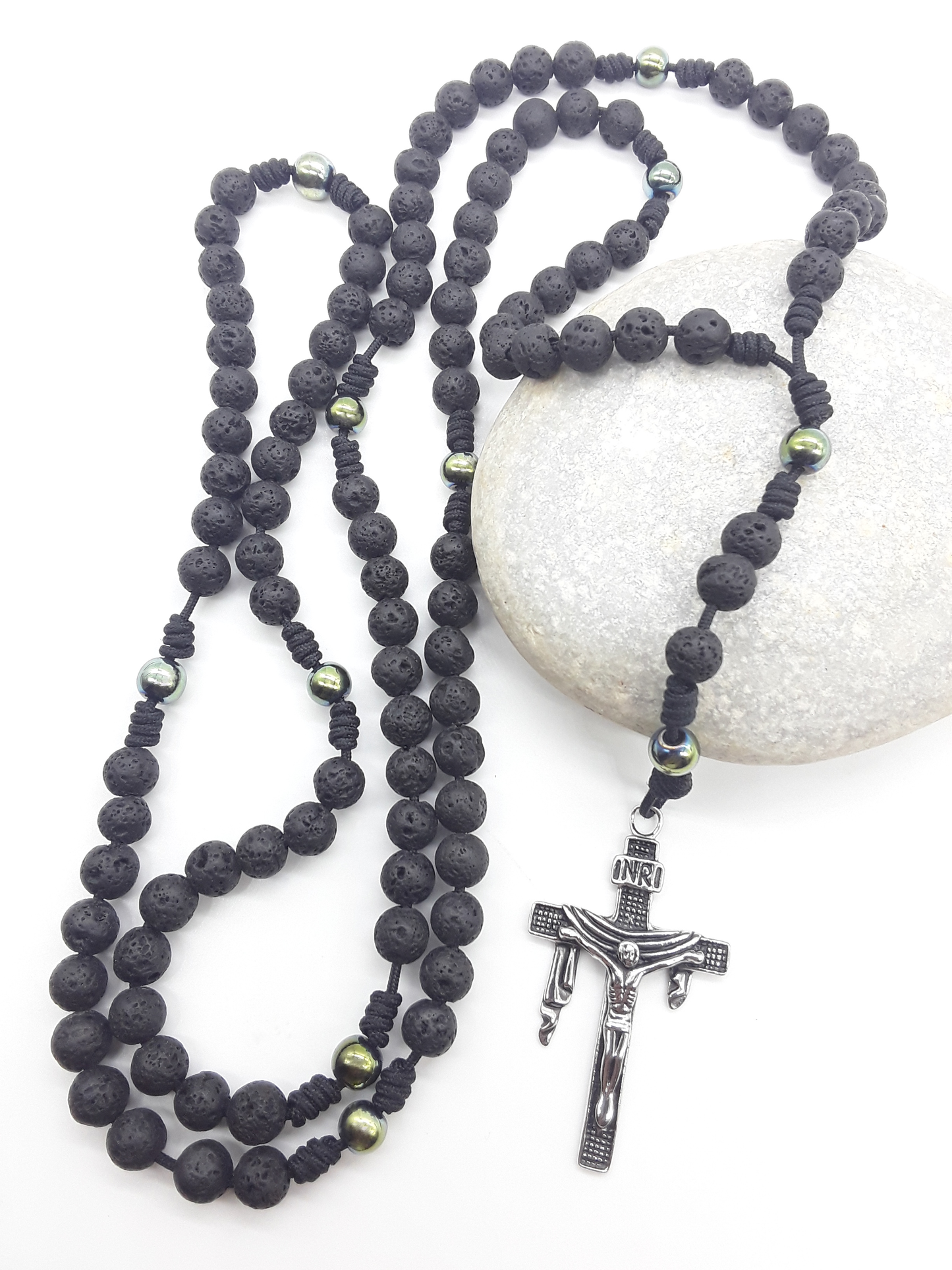 Steadfast Path lava stone and hematite 10-decade Catholic rosary with stainless steel crucifix resting on stone by Polmadeva