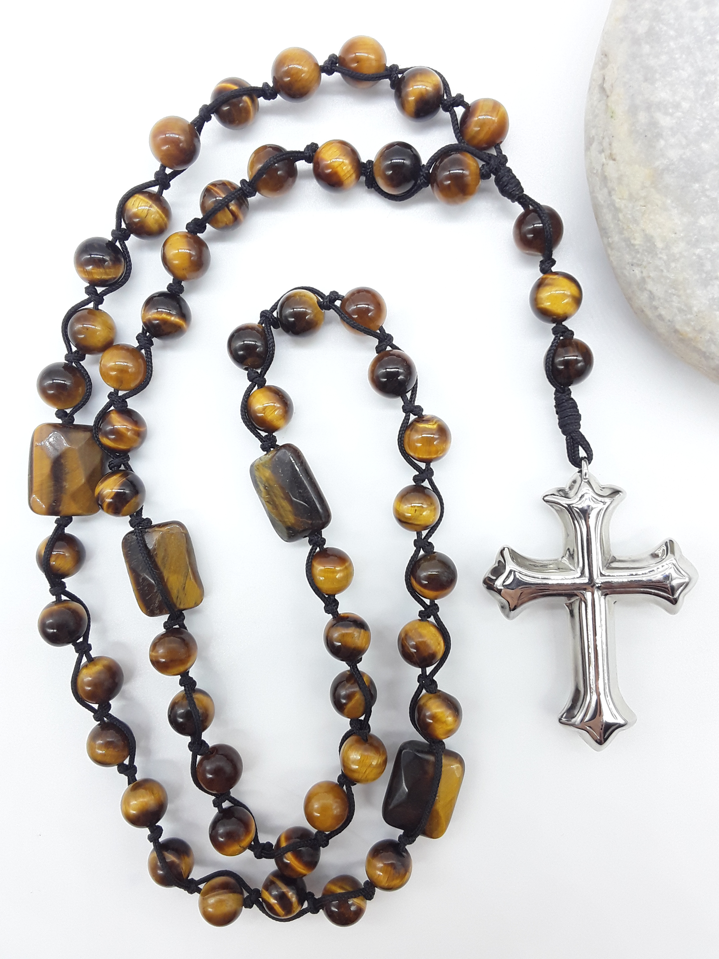 Steady Flame — Tiger’s Eye Catholic Rosary (10 Decade) by Polmadeva placed beside natural stone with stainless steel cross.