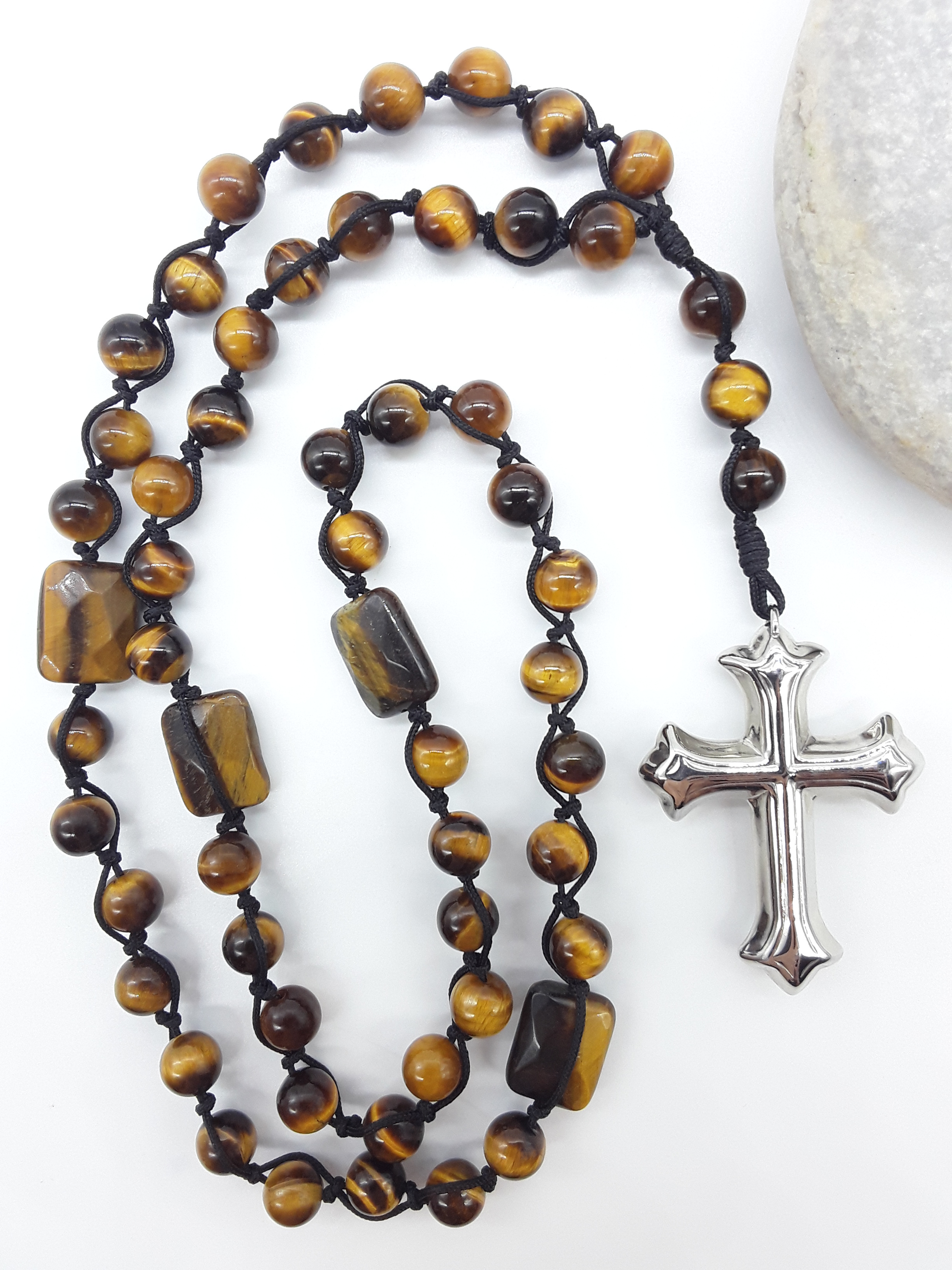 Steady Flame — Tiger’s Eye Catholic Rosary (10 Decade) by Polmadeva placed beside natural stone with stainless steel cross.