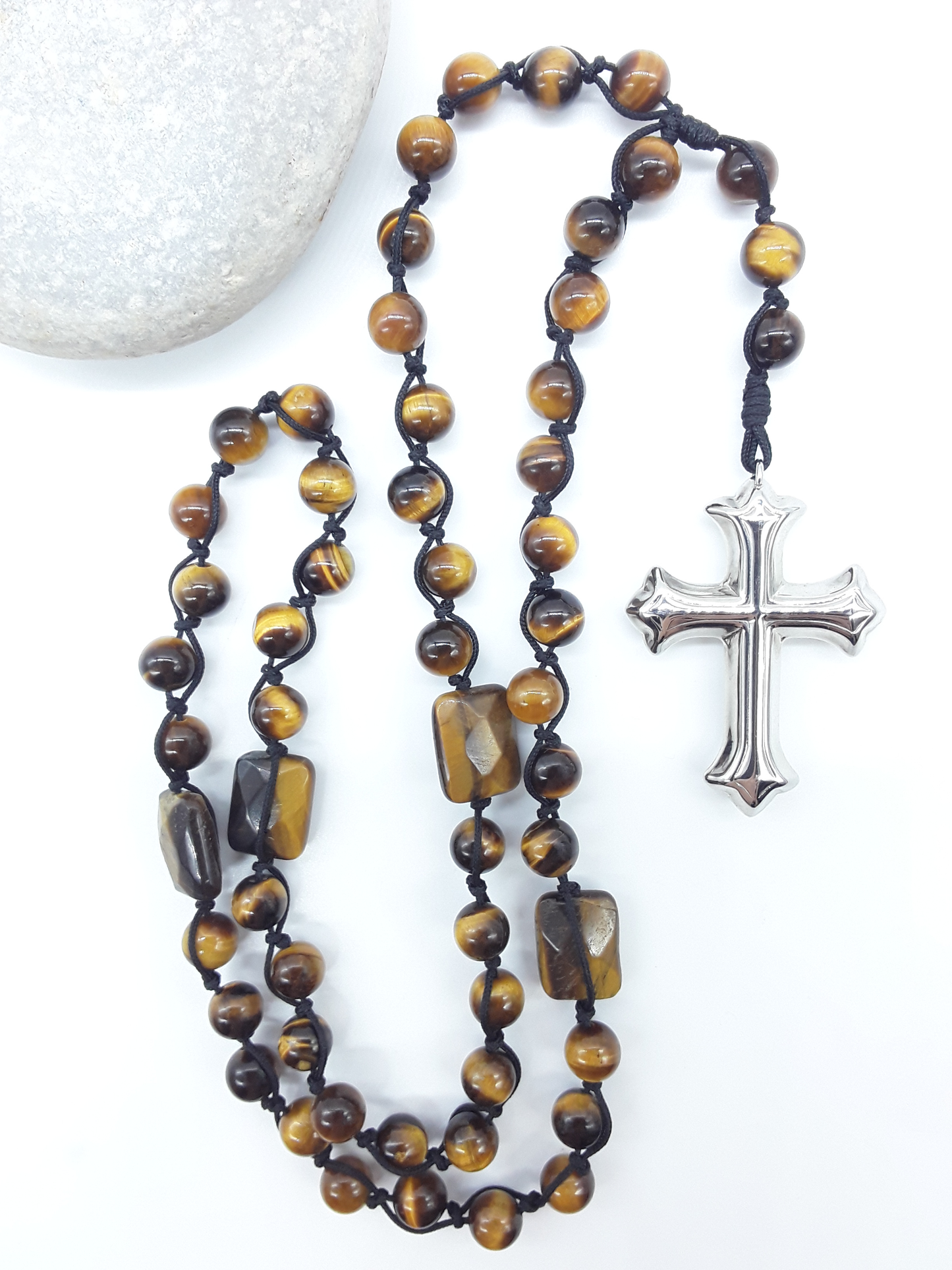 Steady Flame — Tiger’s Eye Catholic Rosary (10 Decade) by Polmadeva placed beside natural stone with stainless steel cross.