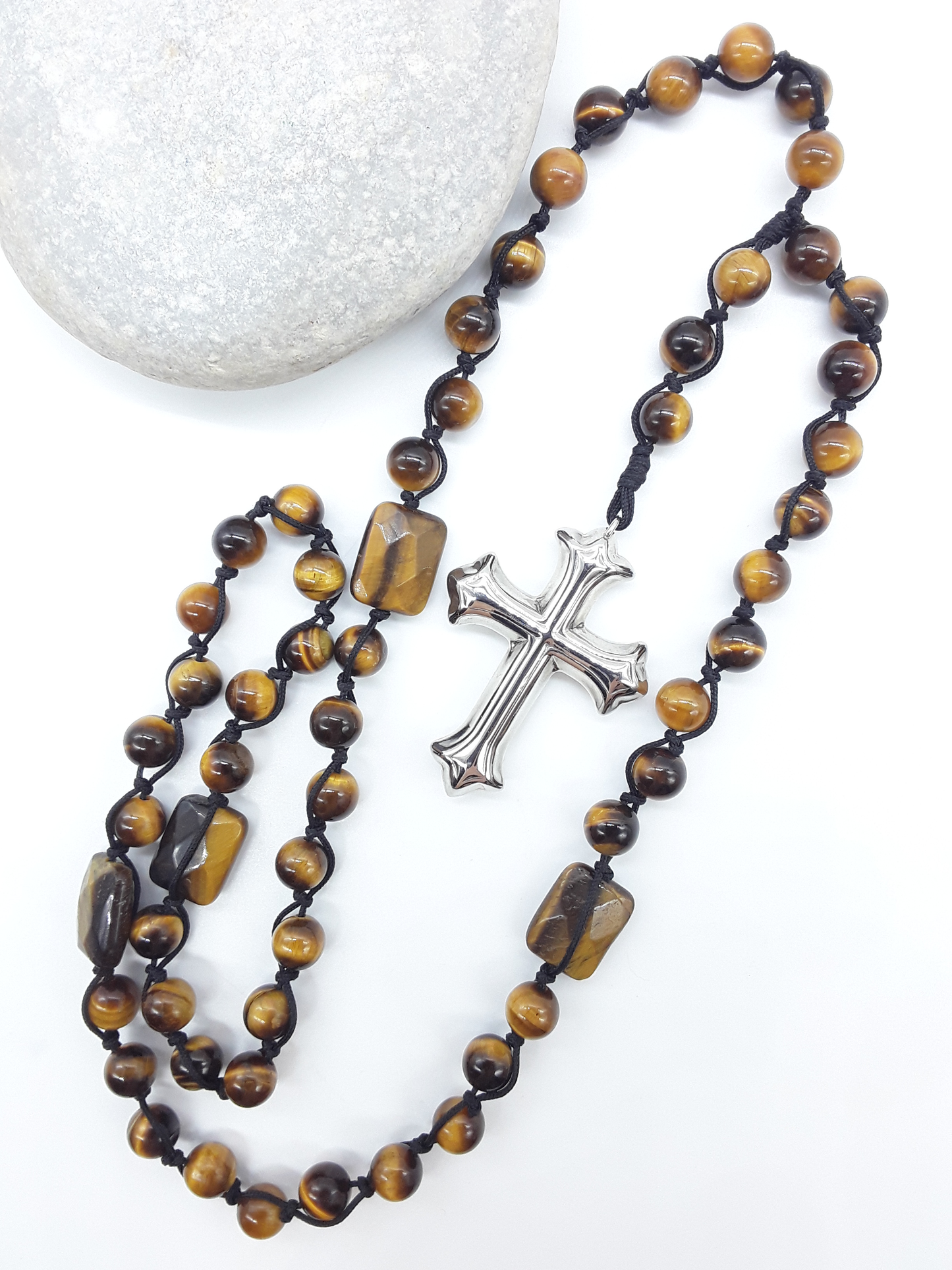 Steady Flame — Tiger’s Eye Catholic Rosary (10 Decade) by Polmadeva placed beside natural stone with stainless steel cross.