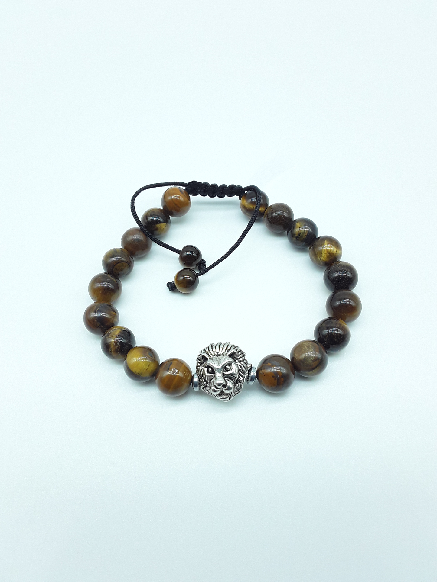 Stillbound bracelet with Tiger’s Eye beads, metal lion element, and adjustable hand-knotted cord on a light background