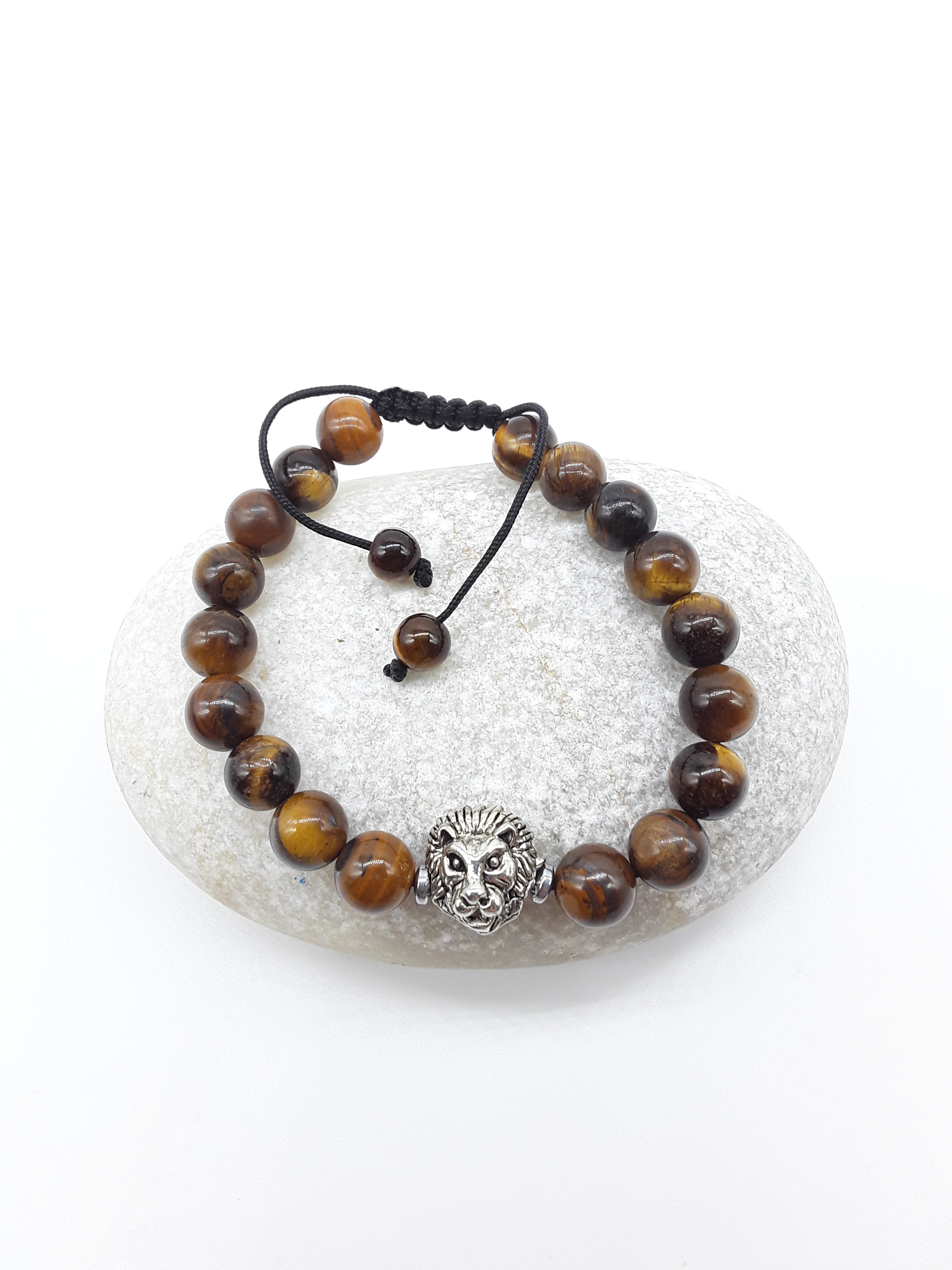Stillbound bracelet with Tiger’s Eye beads, metal lion element, and adjustable hand-knotted cord displayed on a stone surface