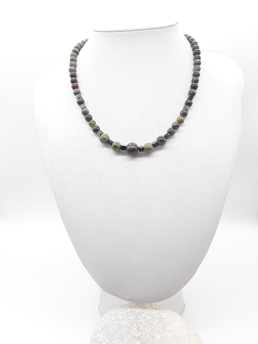 The Emberwake Necklace by Polmadeva displayed on a white bust, handcrafted with Dragon Blood Stone beads in multiple sizes and hematite accents, a Courage Rising talisman awakening inner fire and resilience.