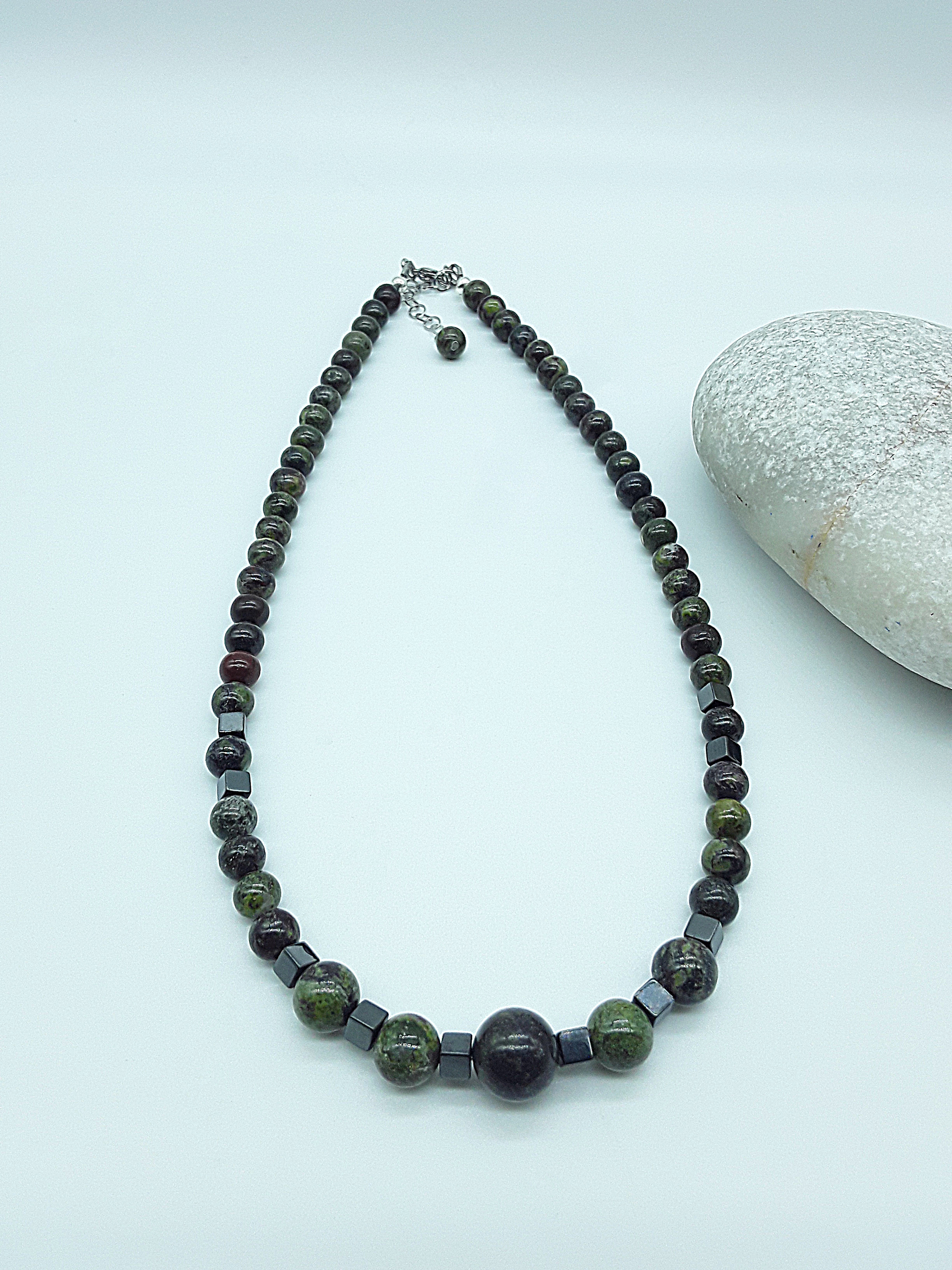The Emberwake Necklace by Polmadeva laid flat on a light background with stone accent, handcrafted with Dragon Blood Stone beads and hematite cubes, a Courage Rising talisman symbolizing awakened inner fire, strength, and resilience.