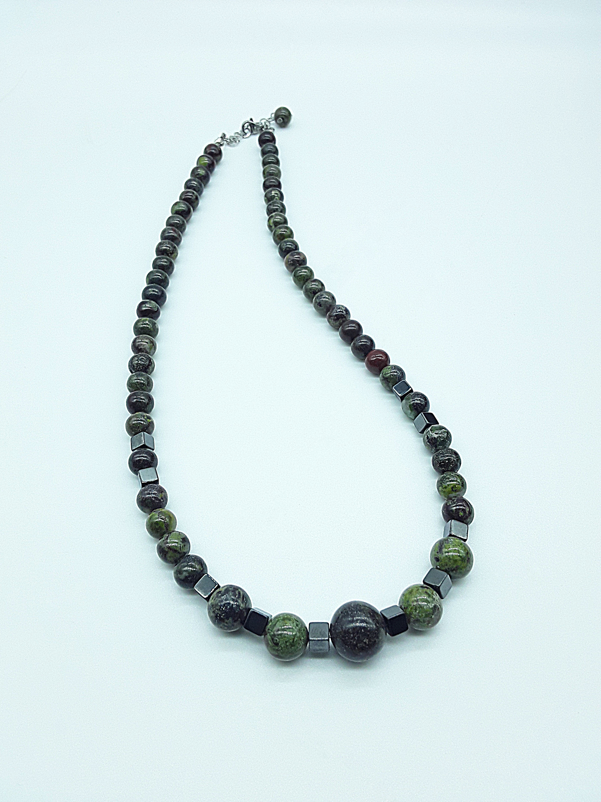 The Emberwake Necklace by Polmadeva resting on a light background, handcrafted with Dragon Blood Stone beads and hematite accents, a Courage Rising talisman symbolizing awakened inner fire, grounded strength, and steady resilience.