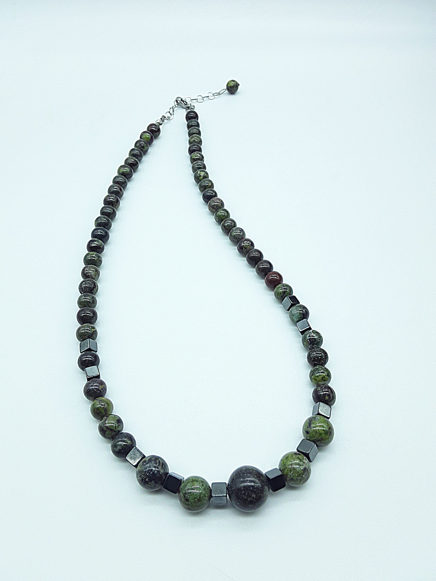 The Emberwake Necklace by Polmadeva resting on a light background, handcrafted with Dragon Blood Stone beads and hematite accents, a Courage Rising talisman symbolizing awakened inner fire, grounded strength, and steady resilience.