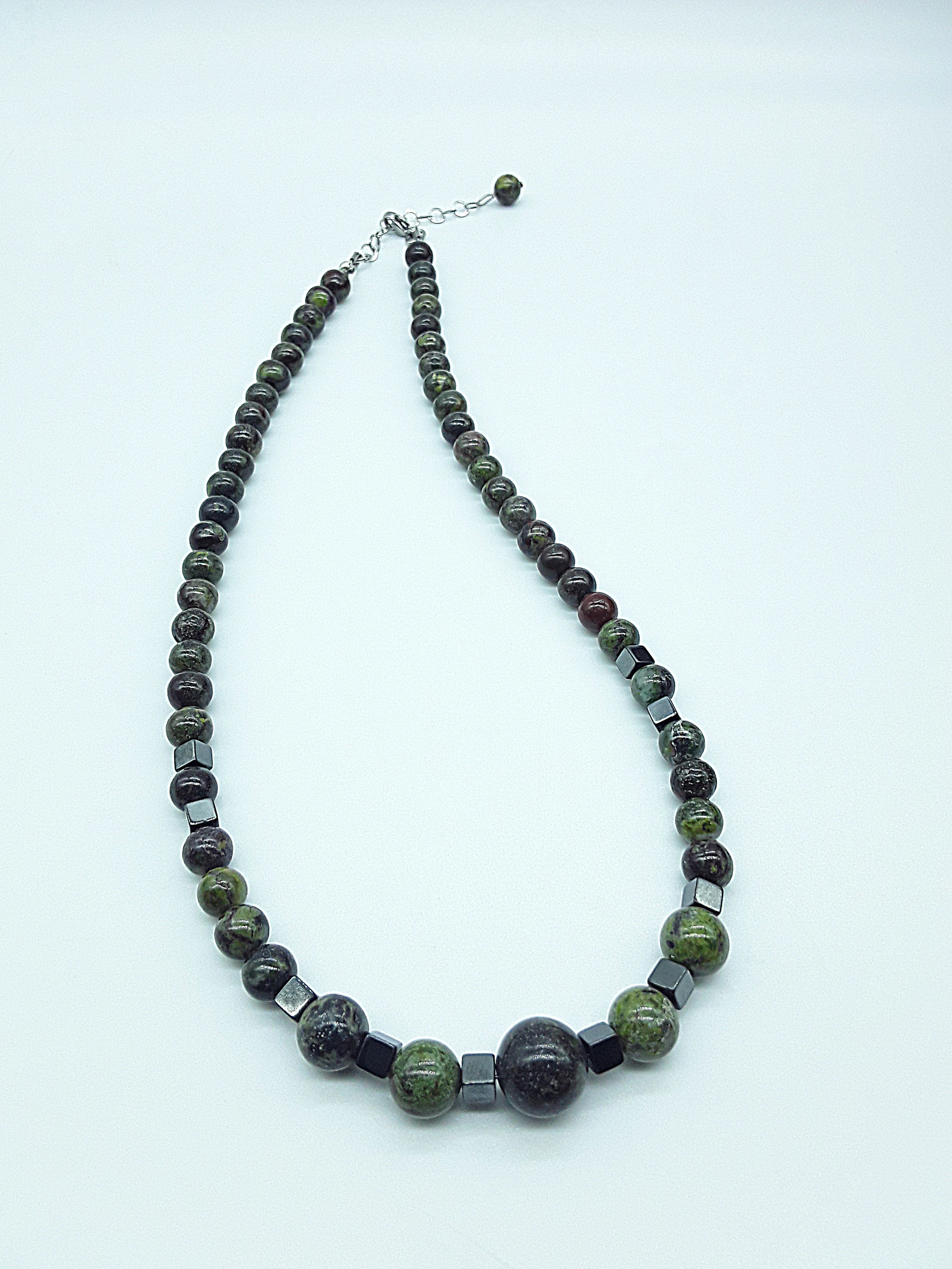 The Emberwake Necklace by Polmadeva resting on a light background, handcrafted with Dragon Blood Stone beads and hematite accents, a Courage Rising talisman symbolizing awakened inner fire, grounded strength, and steady resilience.