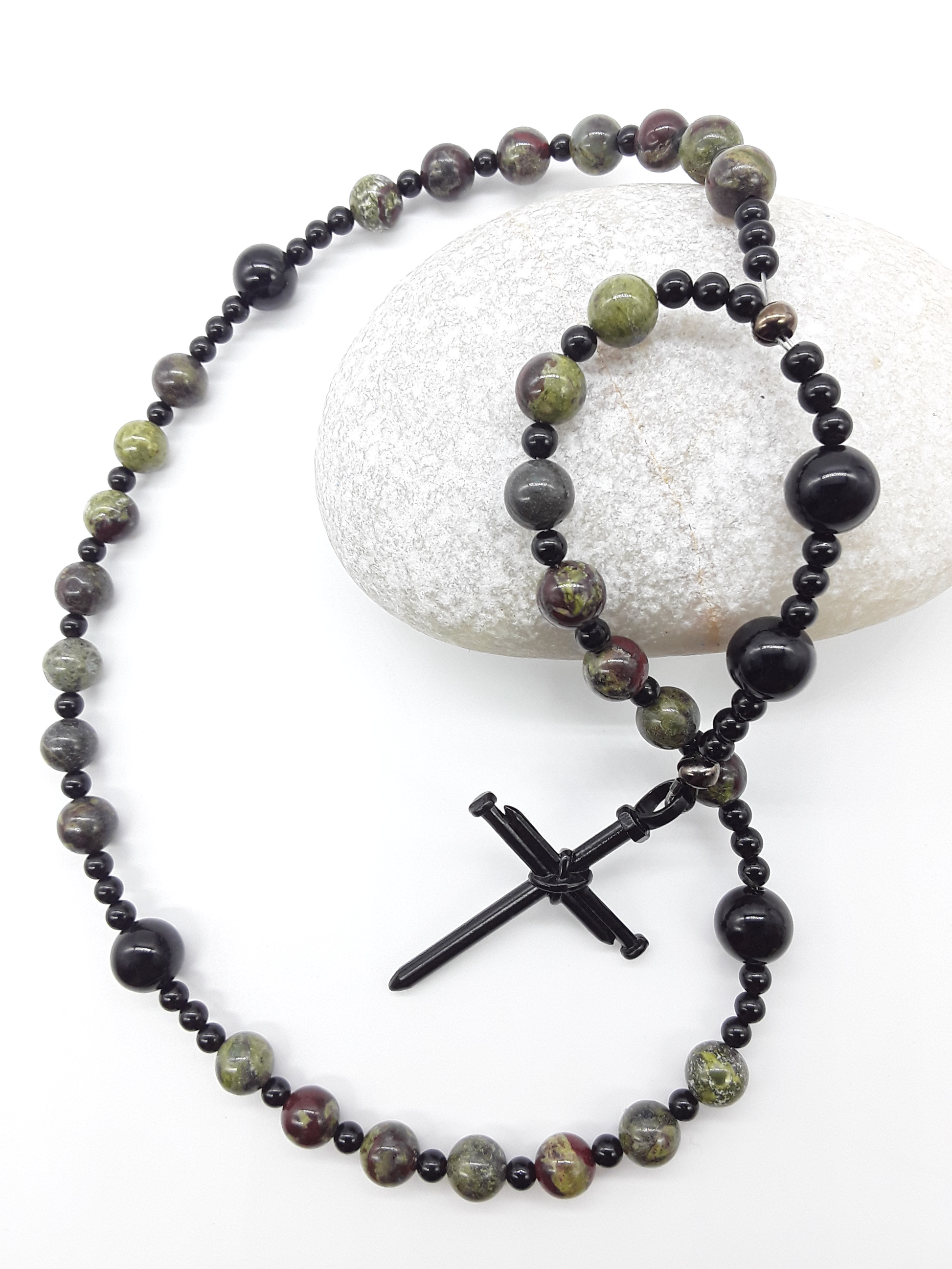 The Enduring Root Anglican Prayer Beads by Polmadeva placed on stone, crafted with Dragon Blood, Black Onyx, and stainless steel nail cross