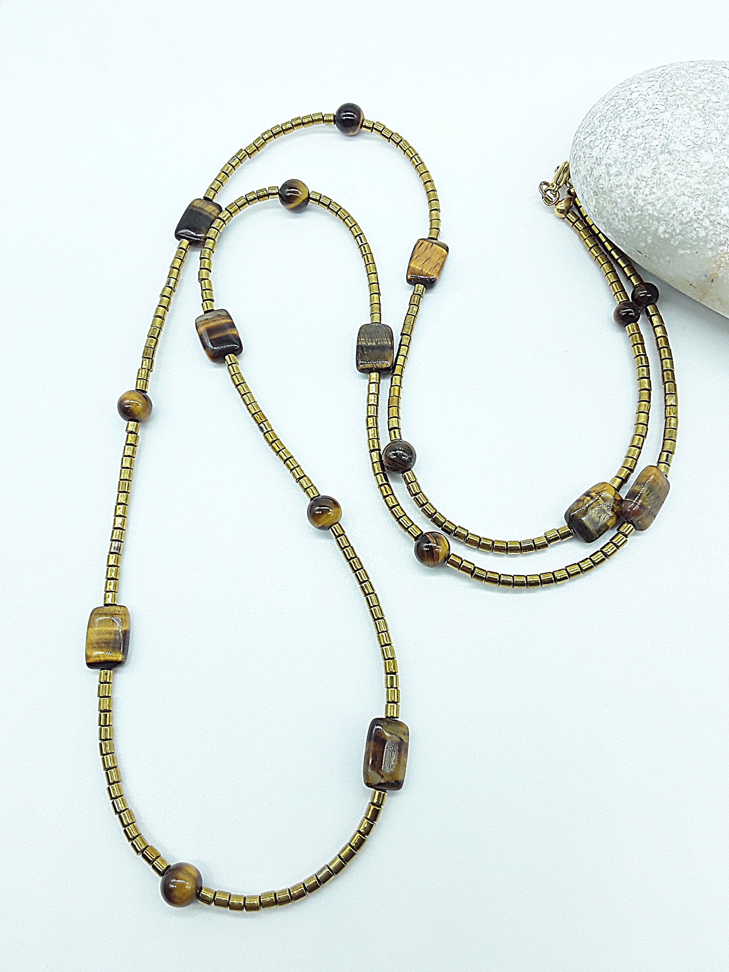 Long gold-toned necklace with mixed Tiger’s Eye bead shapes arranged in a loop on a white background.
