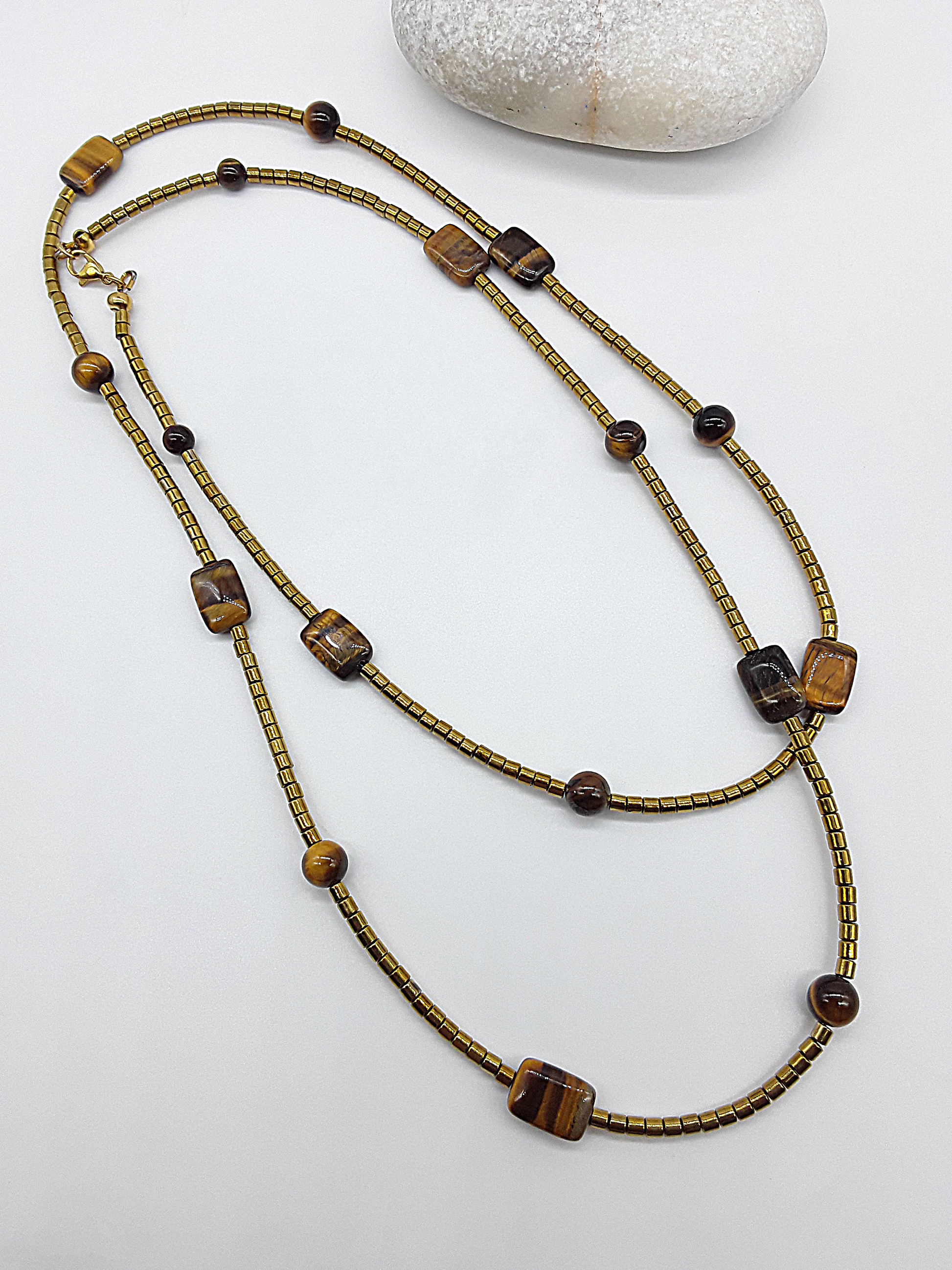 Long gold and brown beaded necklace with Tiger’s Eye and hematite beads arranged loosely on a white surface.