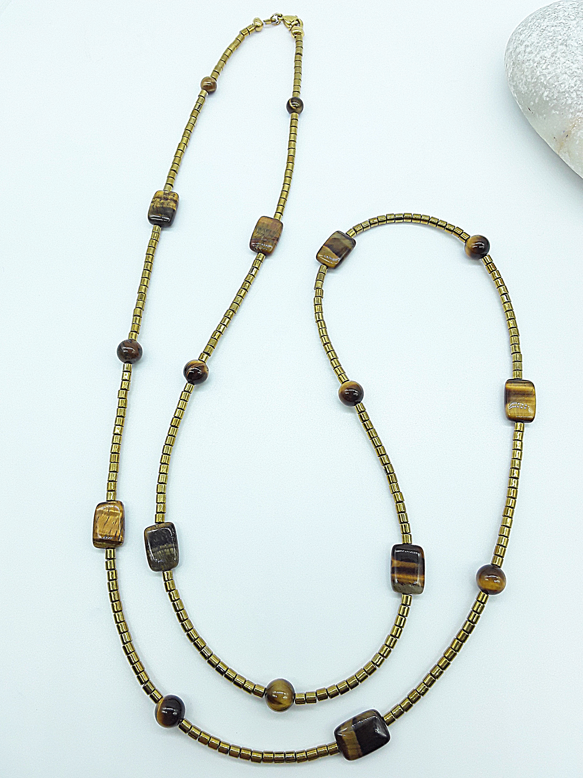 Long gold and brown beaded necklace with Tiger’s Eye and hematite beads arranged loosely on a white surface.