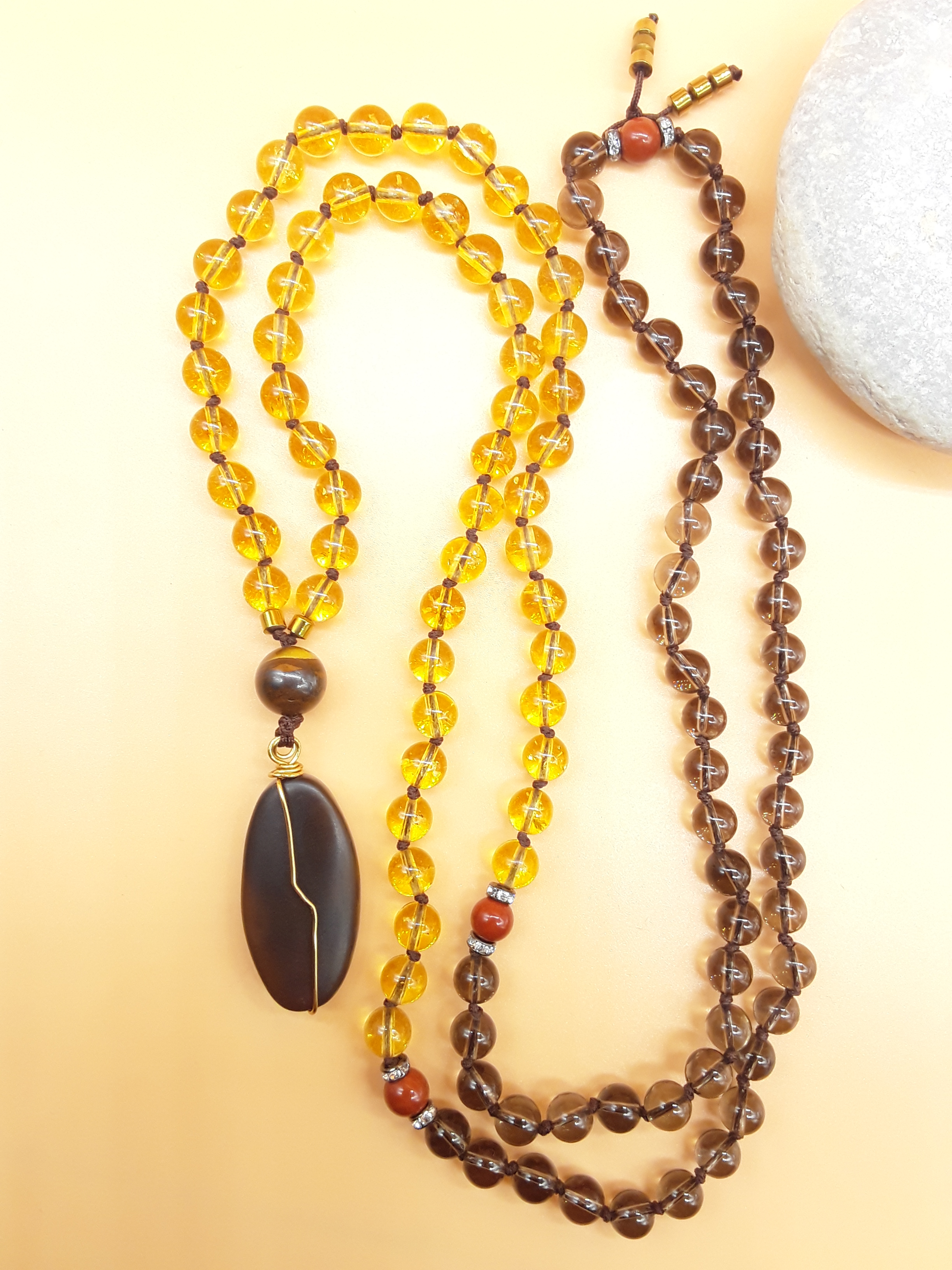Citrine and Smoky Quartz Mala Beads with Agate pendant placed beside white stone on soft background, Polmadeva