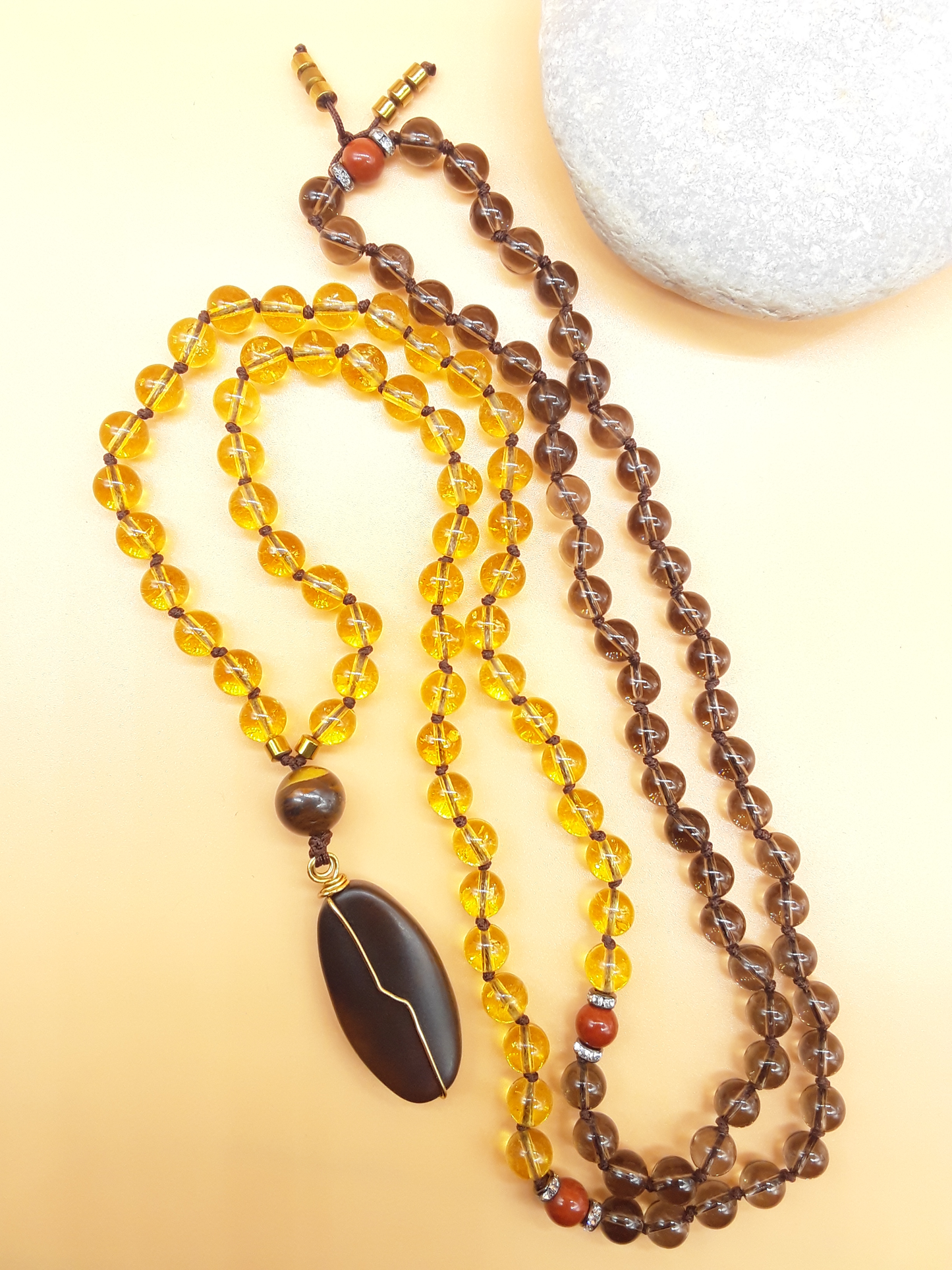 Citrine and Smoky Quartz Mala Beads with Agate pendant placed beside white stone on soft background, Polmadeva