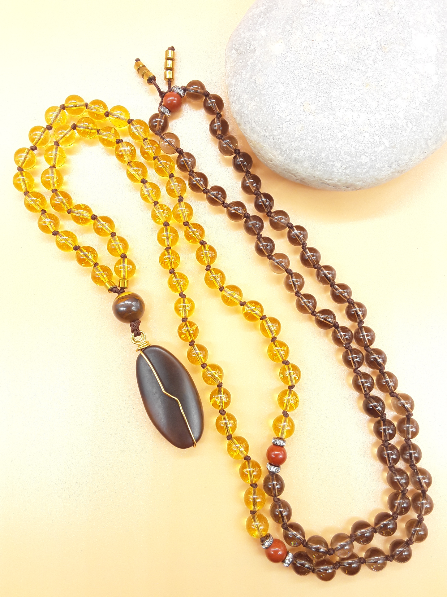 Citrine and Smoky Quartz Mala Beads with Agate pendant placed beside white stone on soft background, Polmadeva