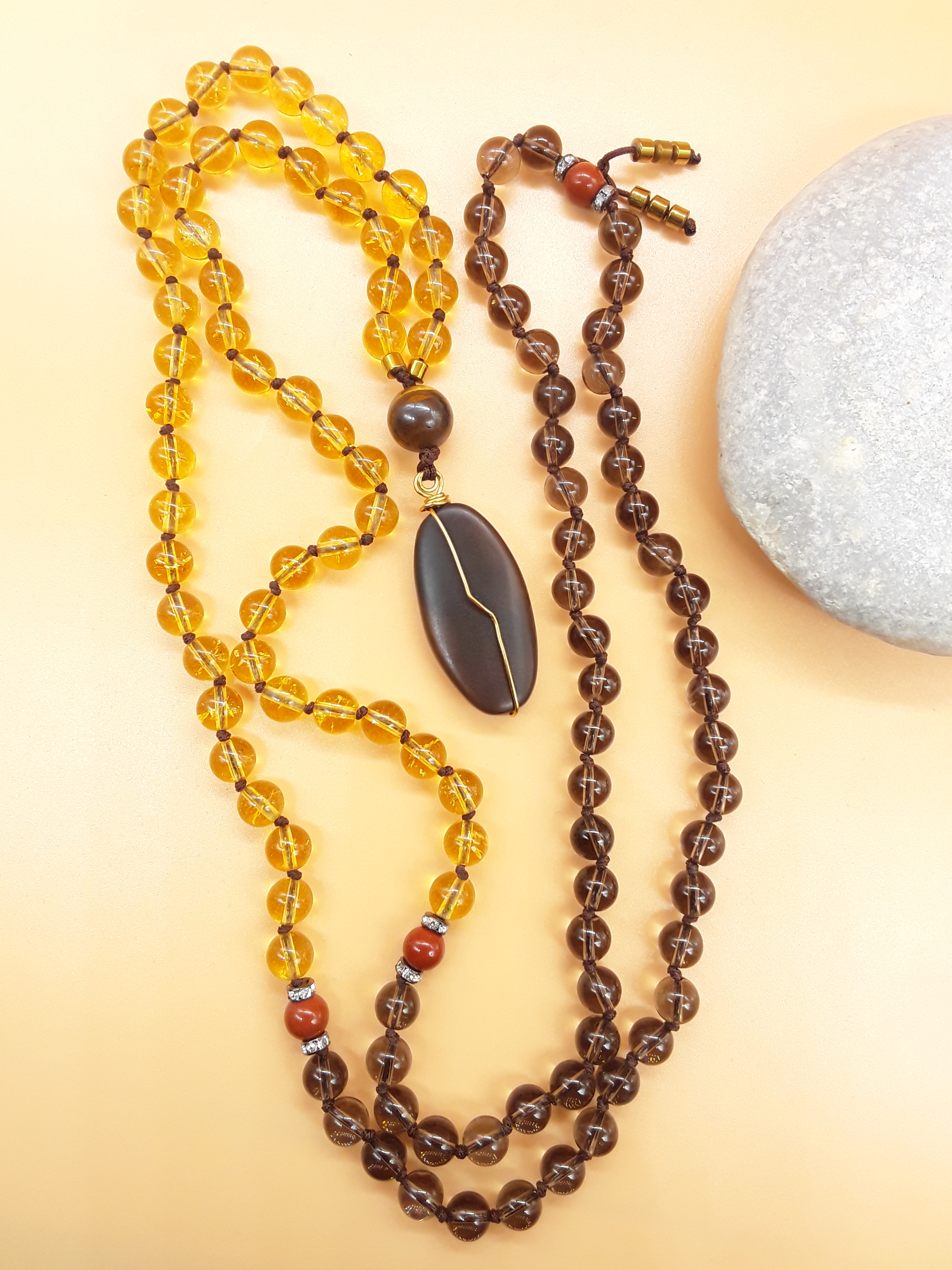 Citrine and Smoky Quartz Mala Beads with Agate pendant placed beside white stone on soft background, Polmadeva