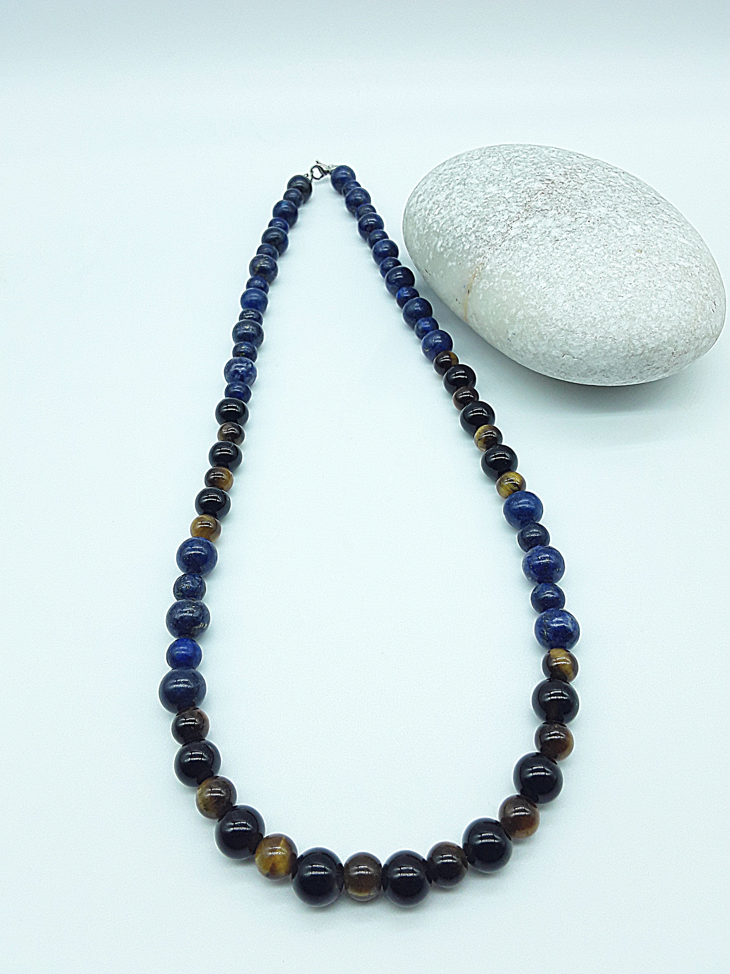 Polmadeva Inner Sight Necklace with lapis lazuli, tiger’s eye and black onyx beads displayed in elongated oval form beside natural stone, Soul Vision collection