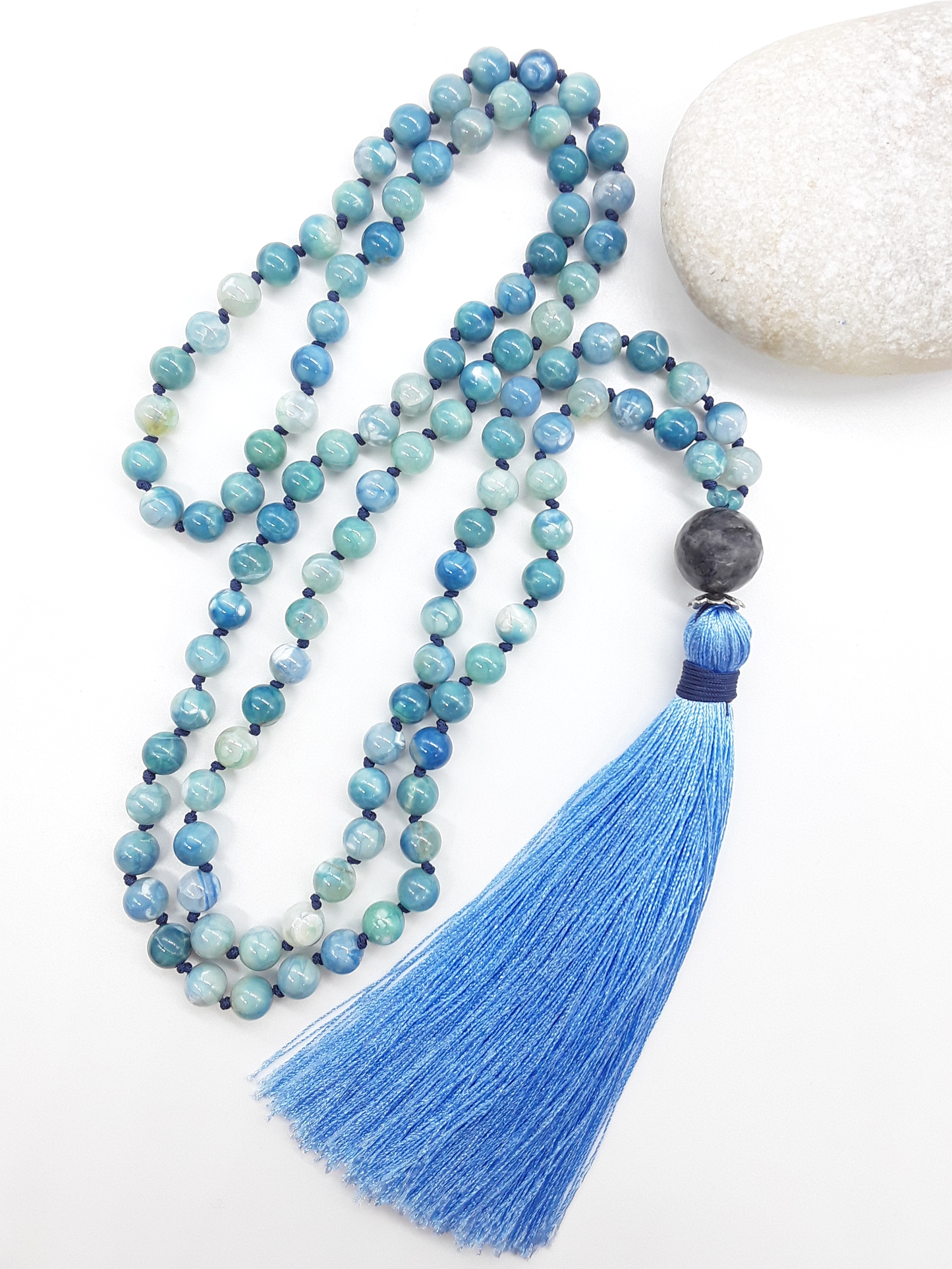 Agate and Labradorite Mala Beads with blue tassel placed beside white stone on white background, Polmadeva
