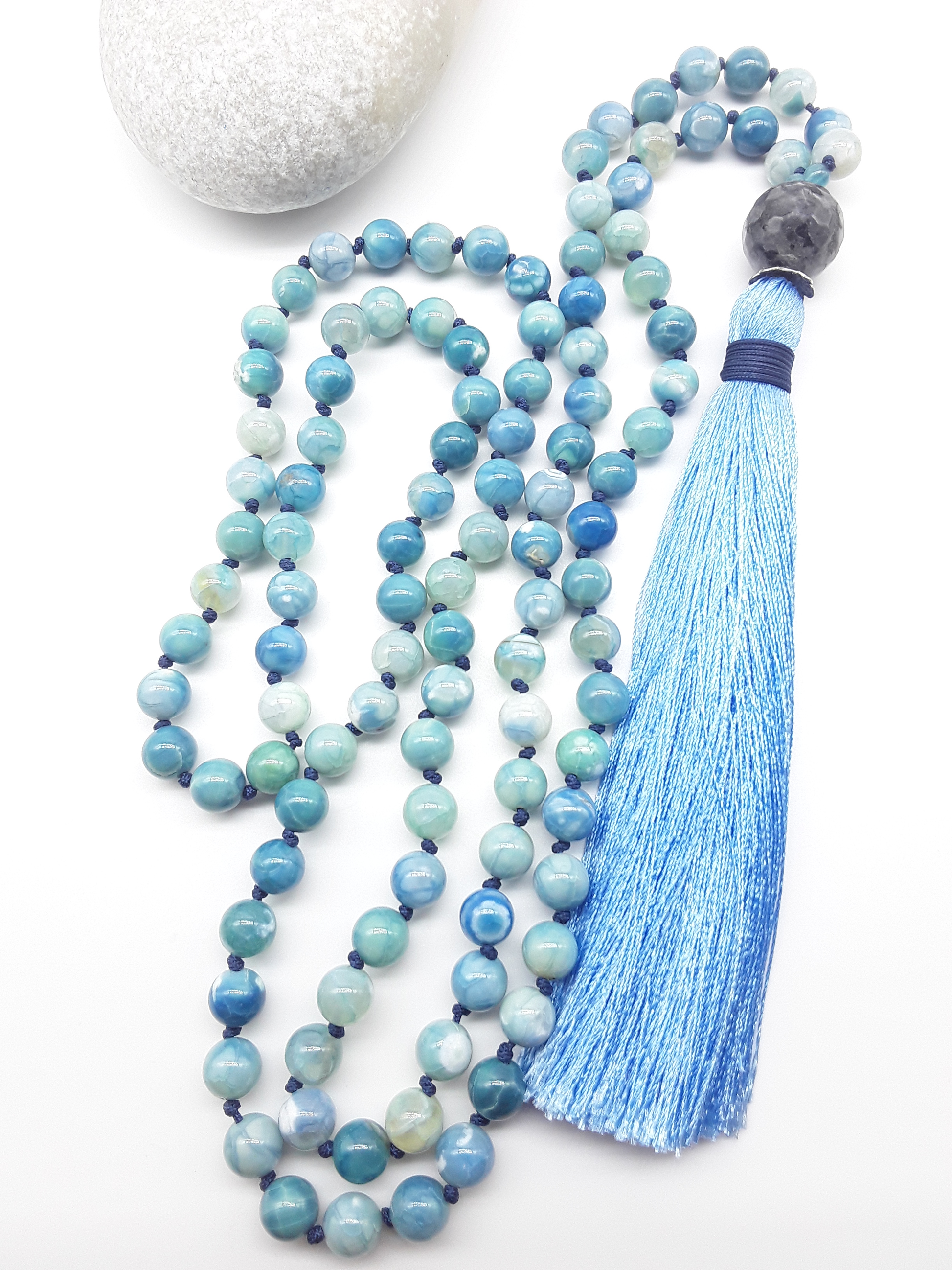 Agate and Labradorite Mala Beads with blue tassel placed beside white stone on white background, Polmadeva