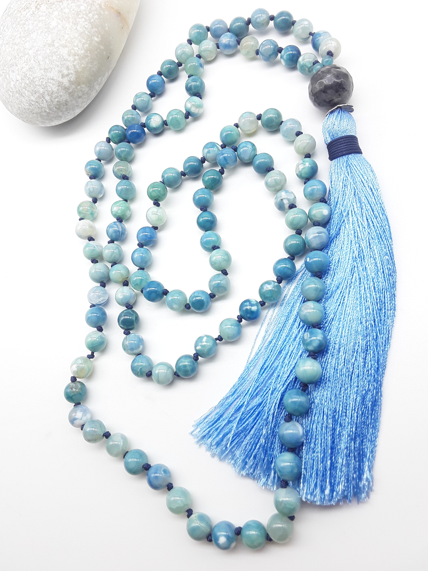 Agate and Labradorite Mala Beads with blue tassel placed beside white stone on white background, Polmadeva
