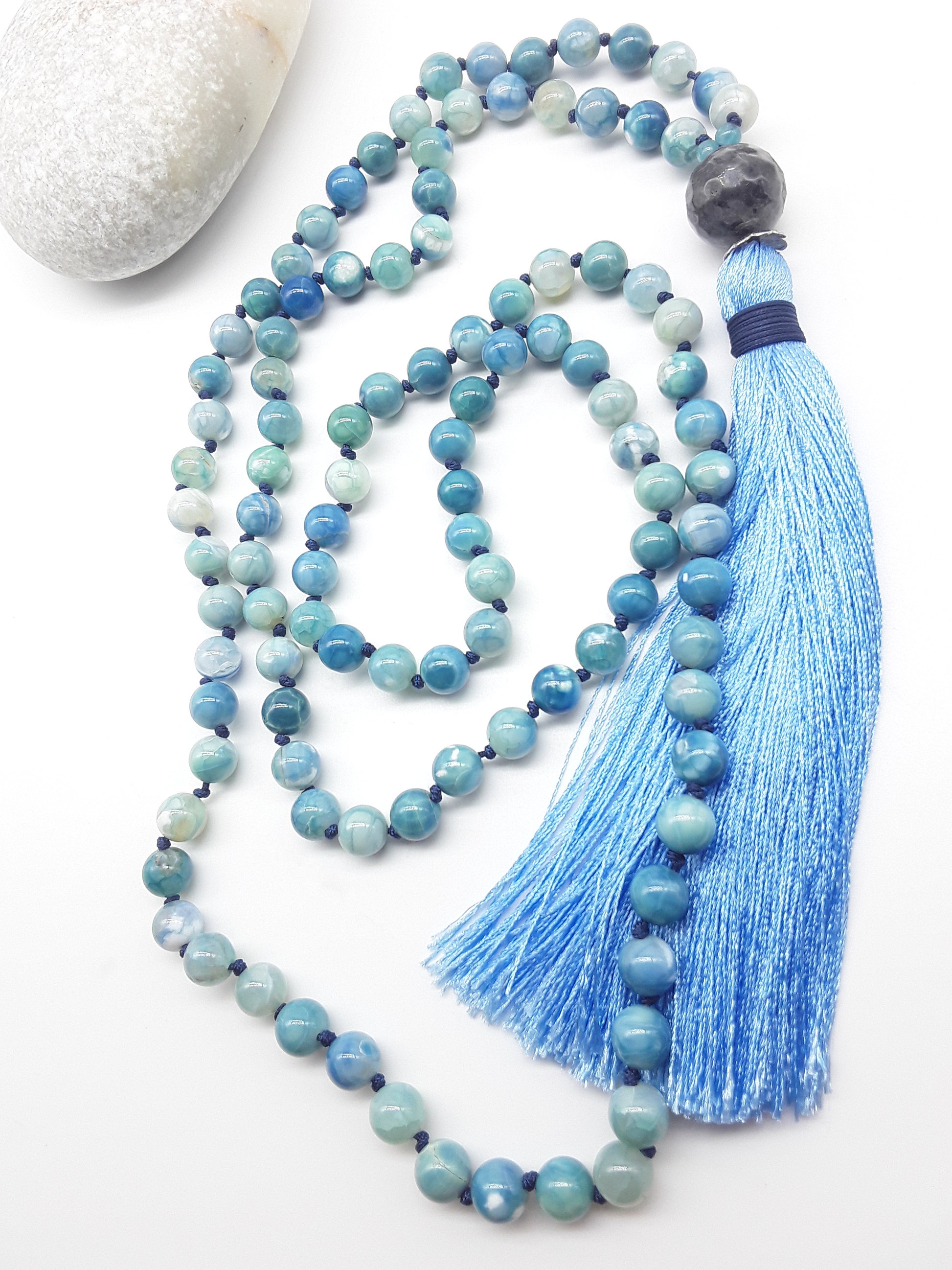 Agate and Labradorite Mala Beads with blue tassel placed beside white stone on white background, Polmadeva