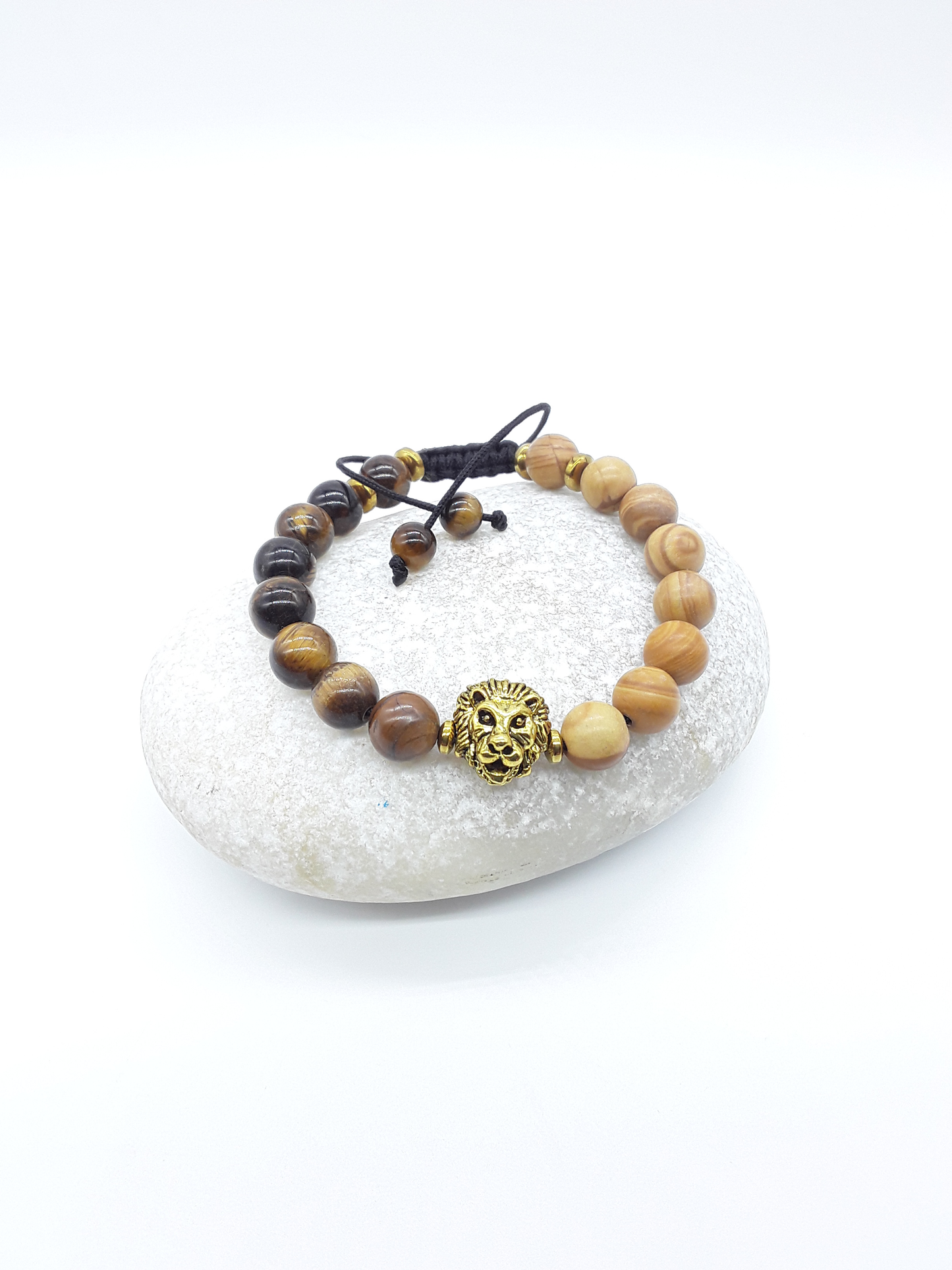 The Kept Ground bracelet with Tiger’s Eye and Jasper beads and gold-toned lion centerpiece resting on natural stone