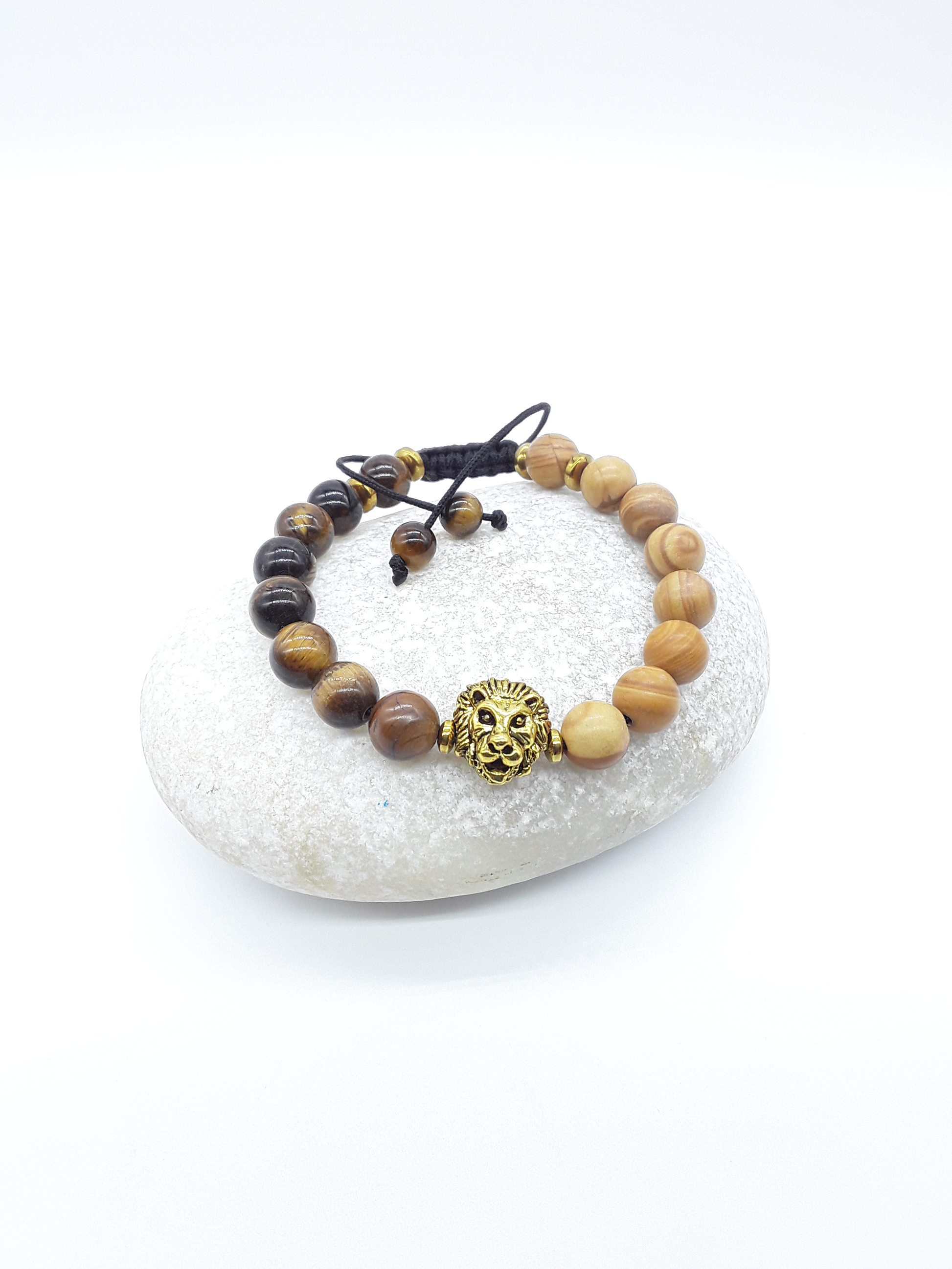 The Kept Ground bracelet with Tiger’s Eye and Jasper beads and gold-toned lion centerpiece resting on natural stone