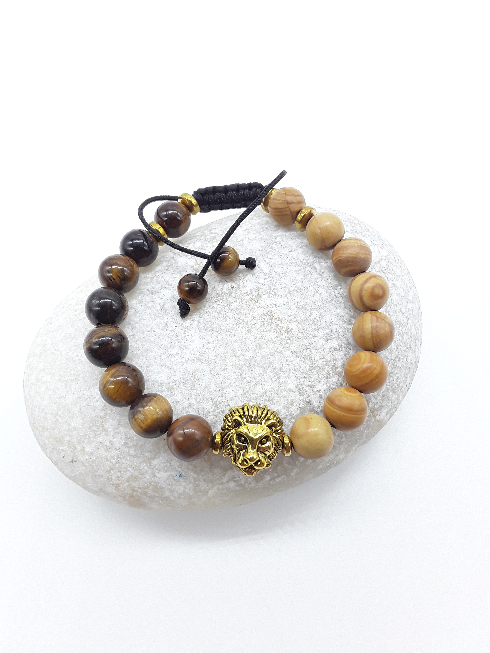 The Kept Ground bracelet with Tiger’s Eye and Jasper beads and gold-toned lion centerpiece resting on natural stone