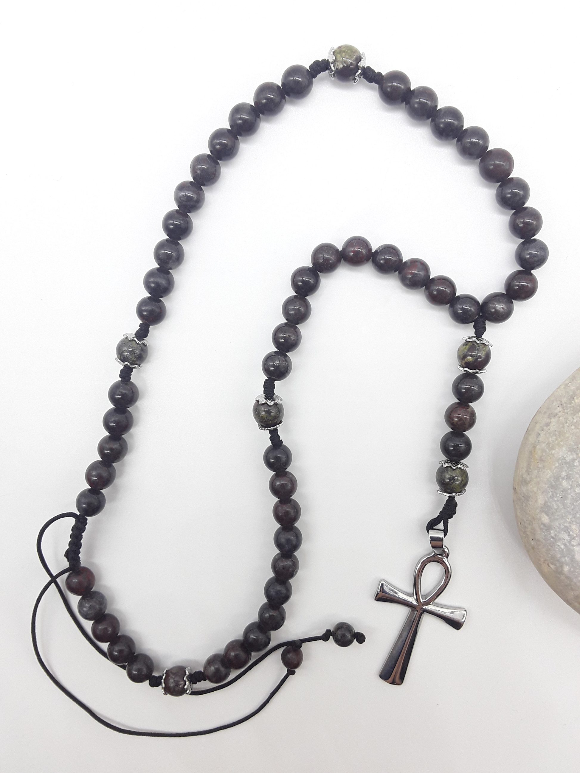 Catholic bloodstone rosary with Ankh cross placed beside natural stone on white surface
